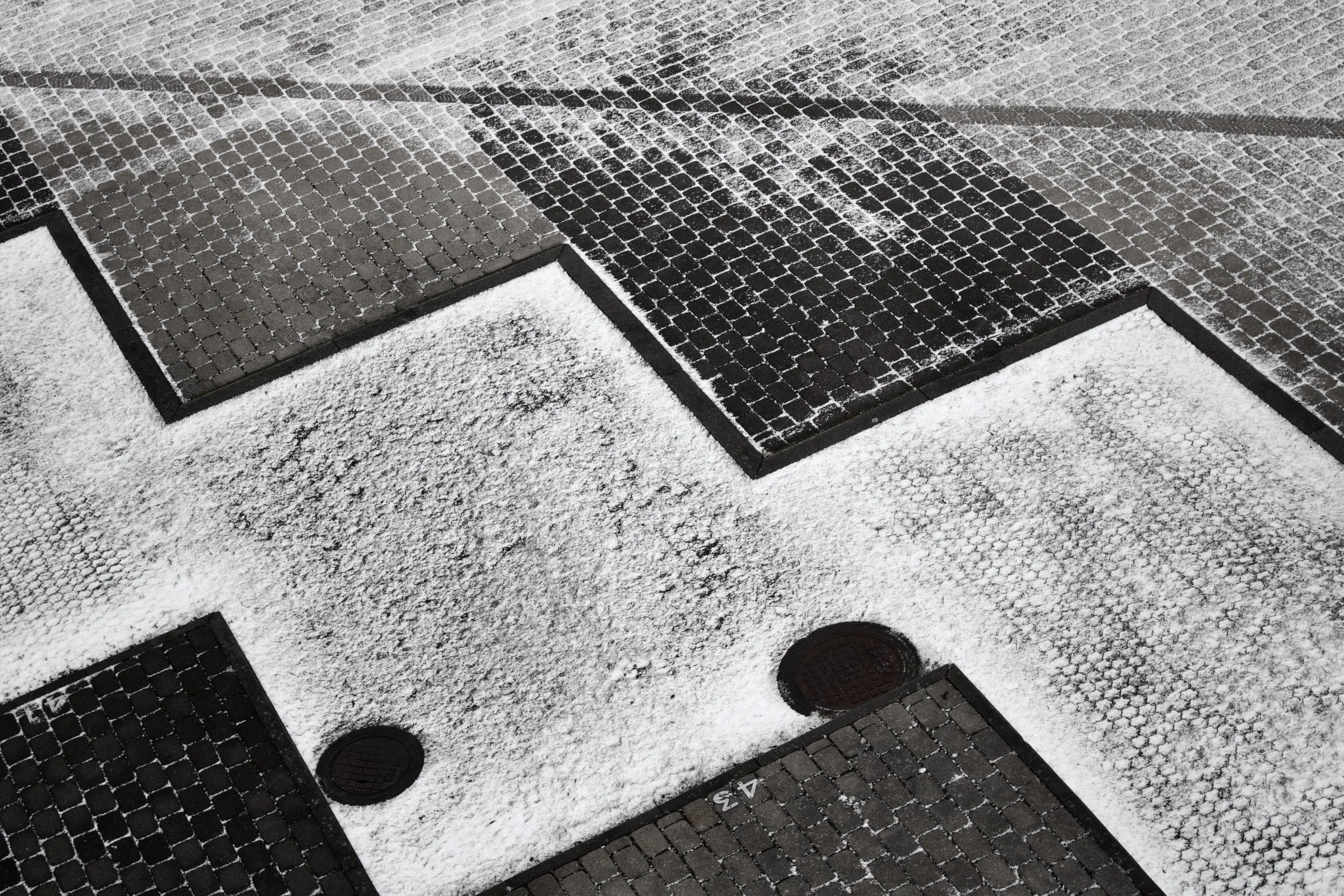 Snow-covered metal grates on a sidewalk with scattered snow and ice patches.