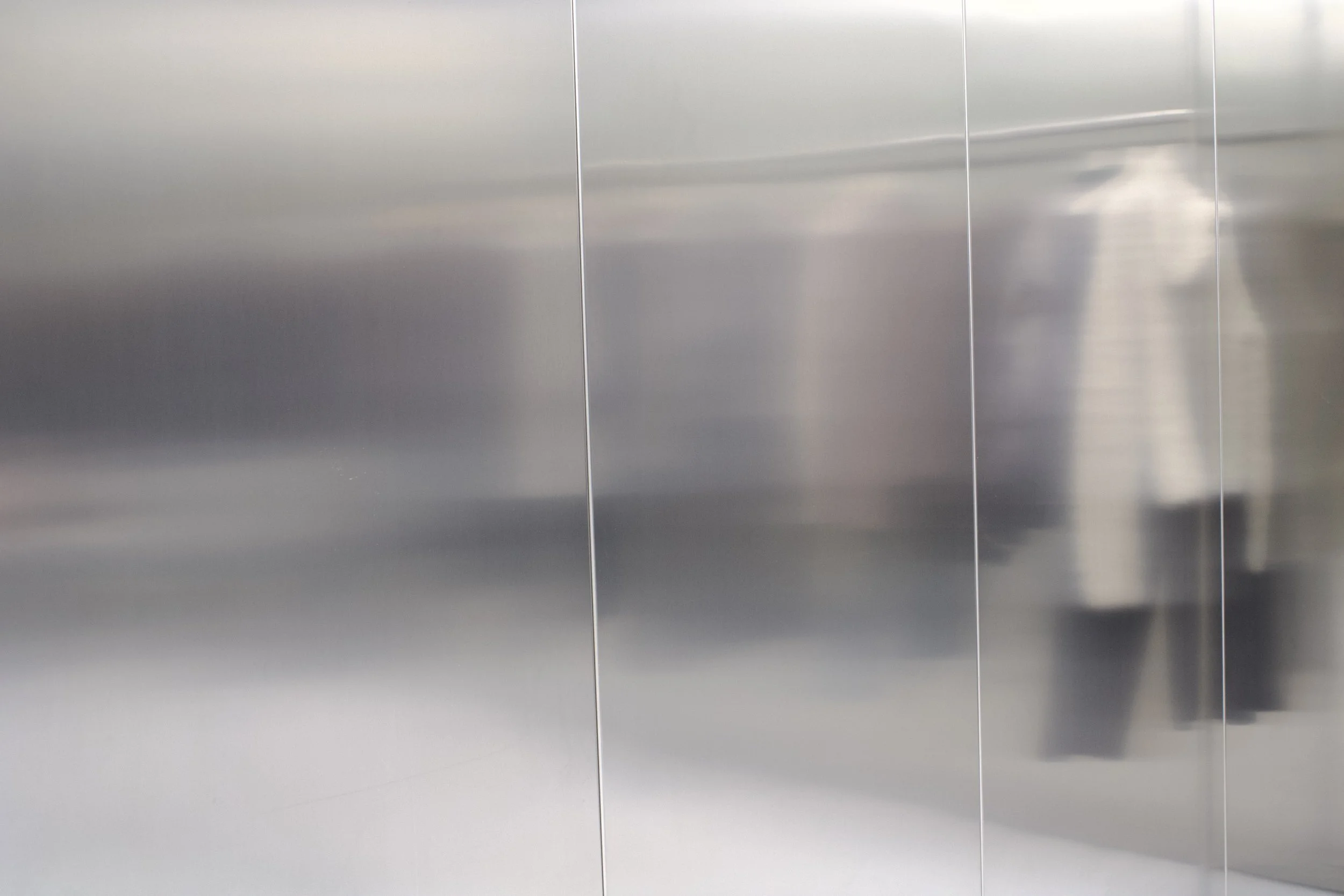A metallic elevator wall with vertical seams.