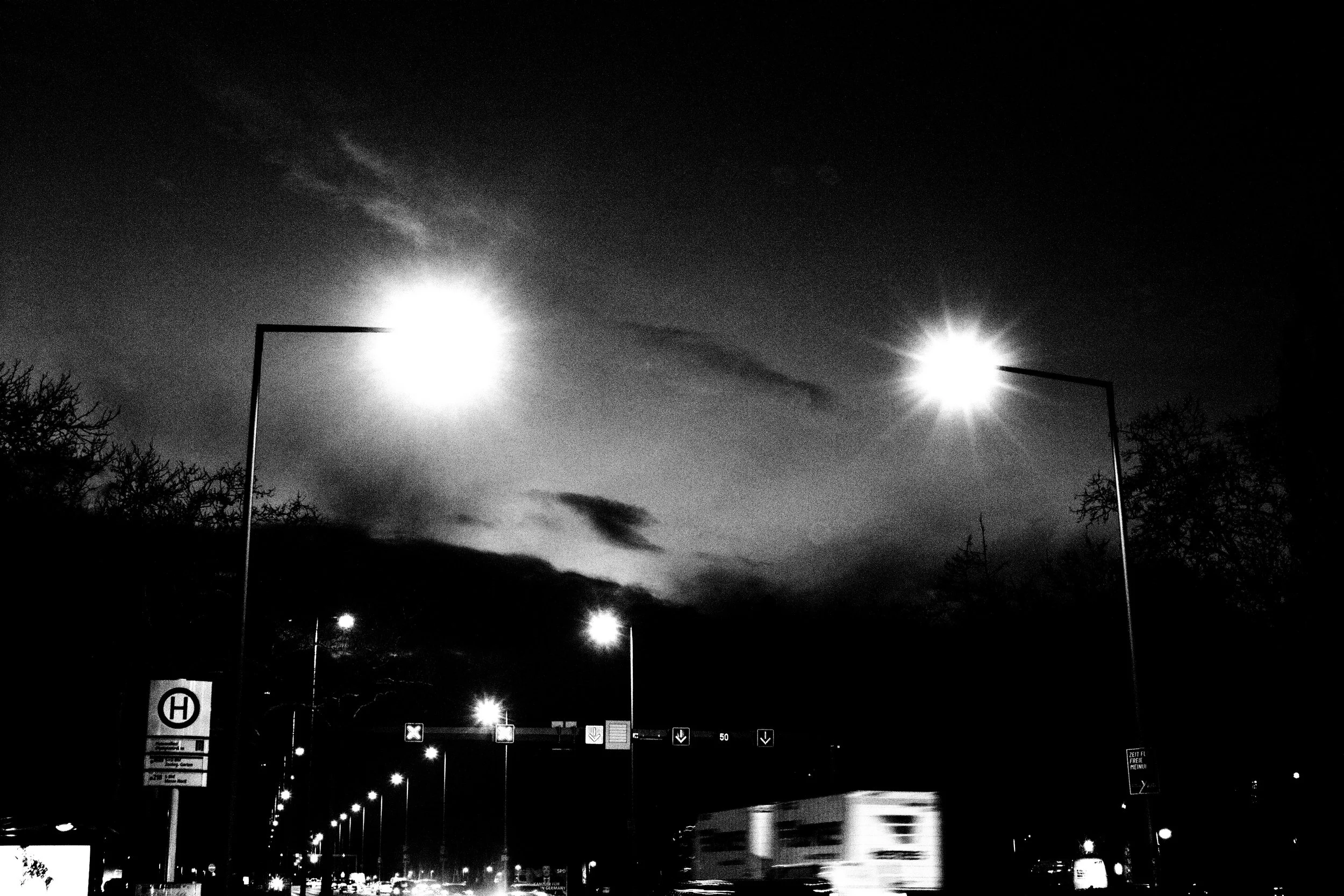 Nighttime city street with illuminated streetlights, visible road signs, and vehicle lights against a dark sky.