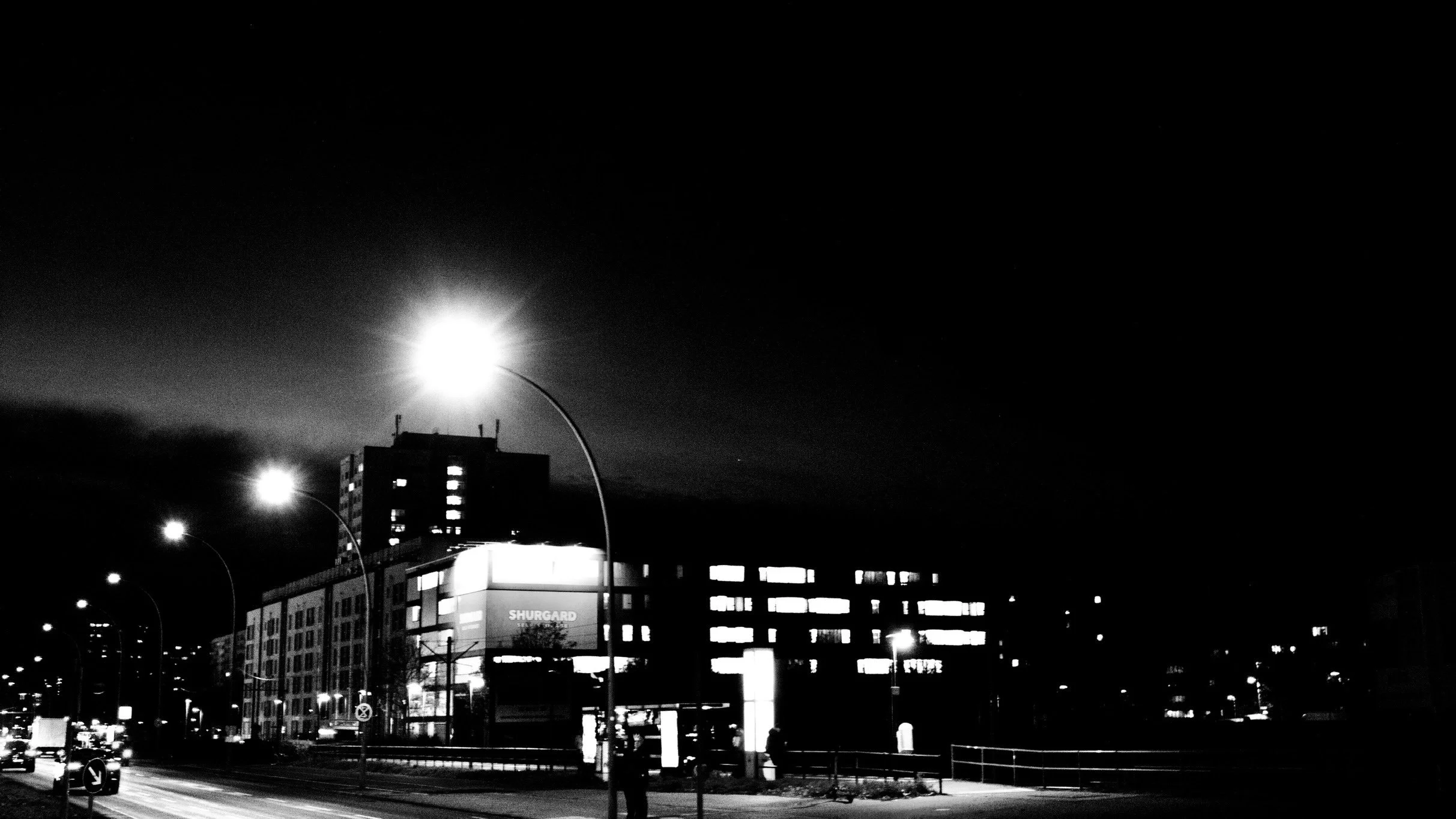 Night cityscape featuring illuminated streetlights, modern buildings, and a person walking on the sidewalk.