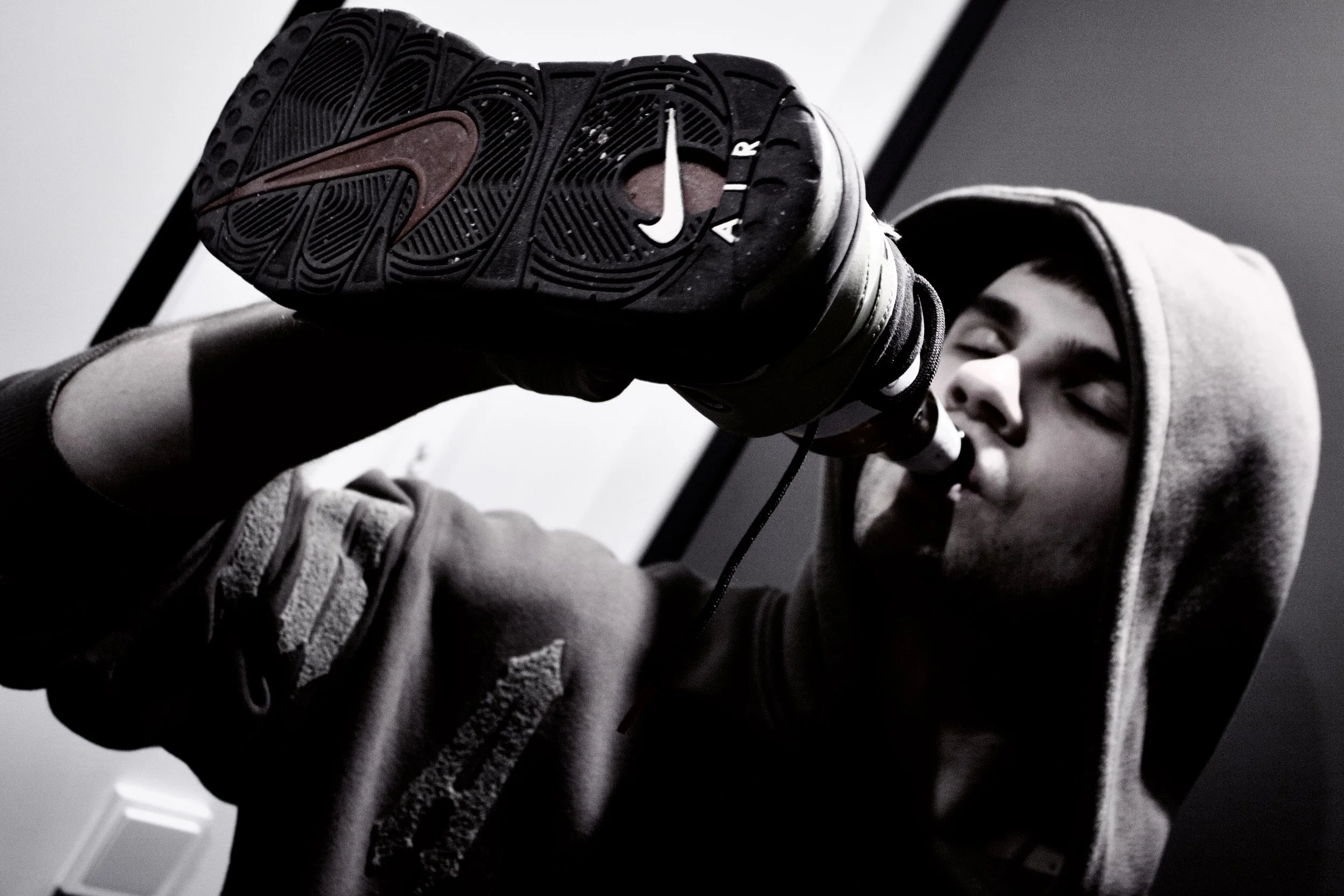 A person in a hoodie holding up a sneaker with the gum sole facing the camera. The sneaker has a visible logo and textured sole.