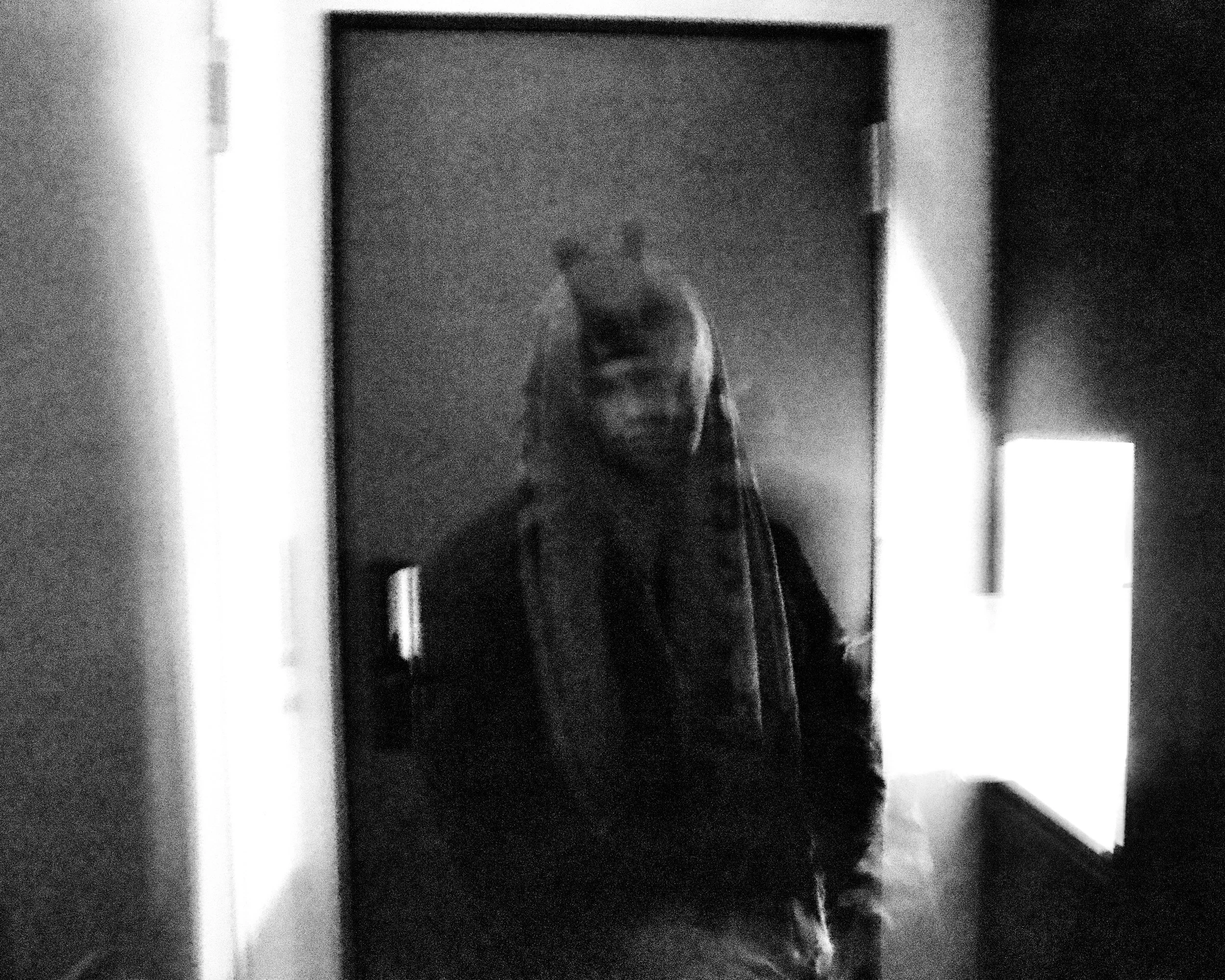 A reflection of a person taking a photo in a mirror, viewed in a grayscale, blurry, low-resolution image.