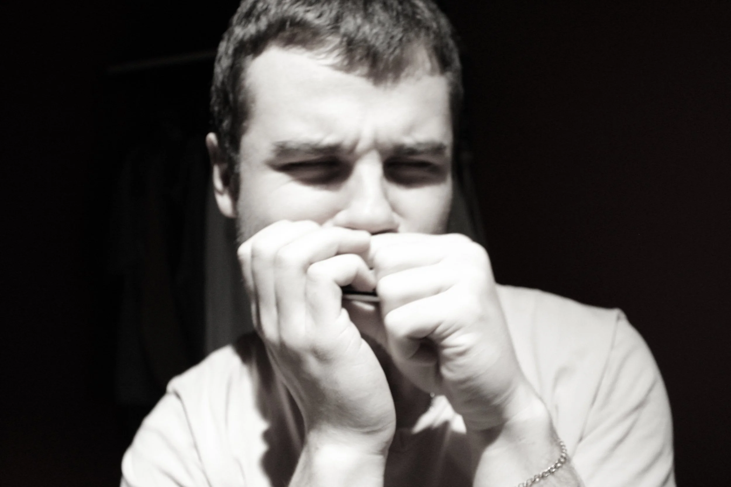 Black and white photo of a person with short hair, holding their hands near their face and squinting.