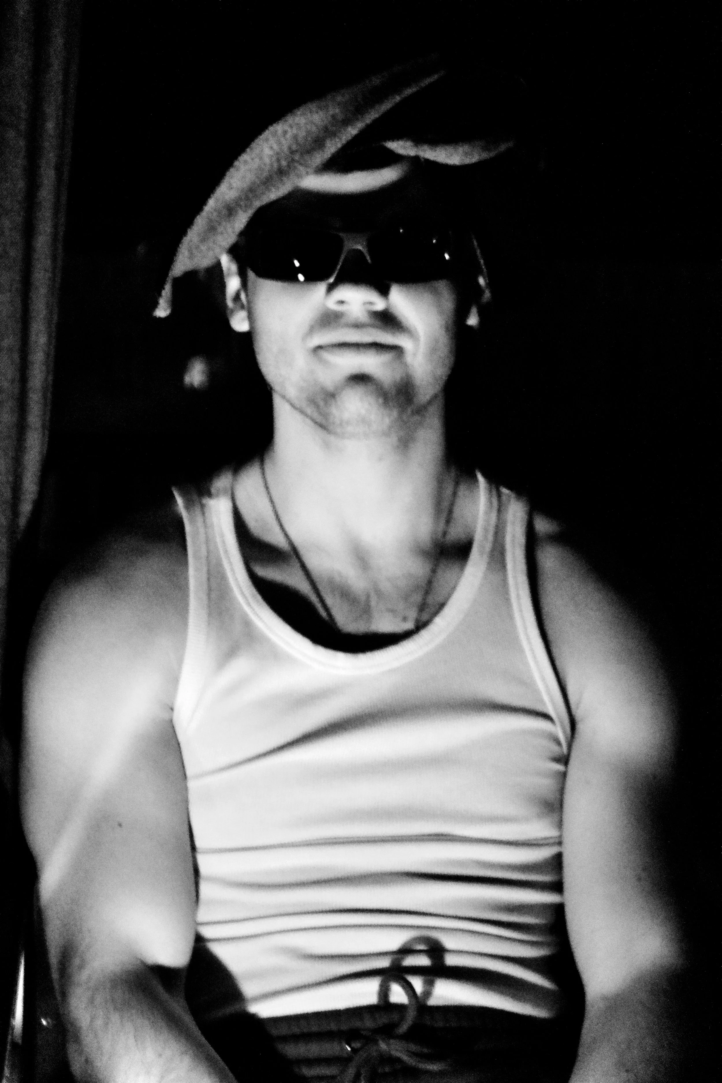 A person wearing sunglasses and a tank top, taking a selfie in a dark environment.
