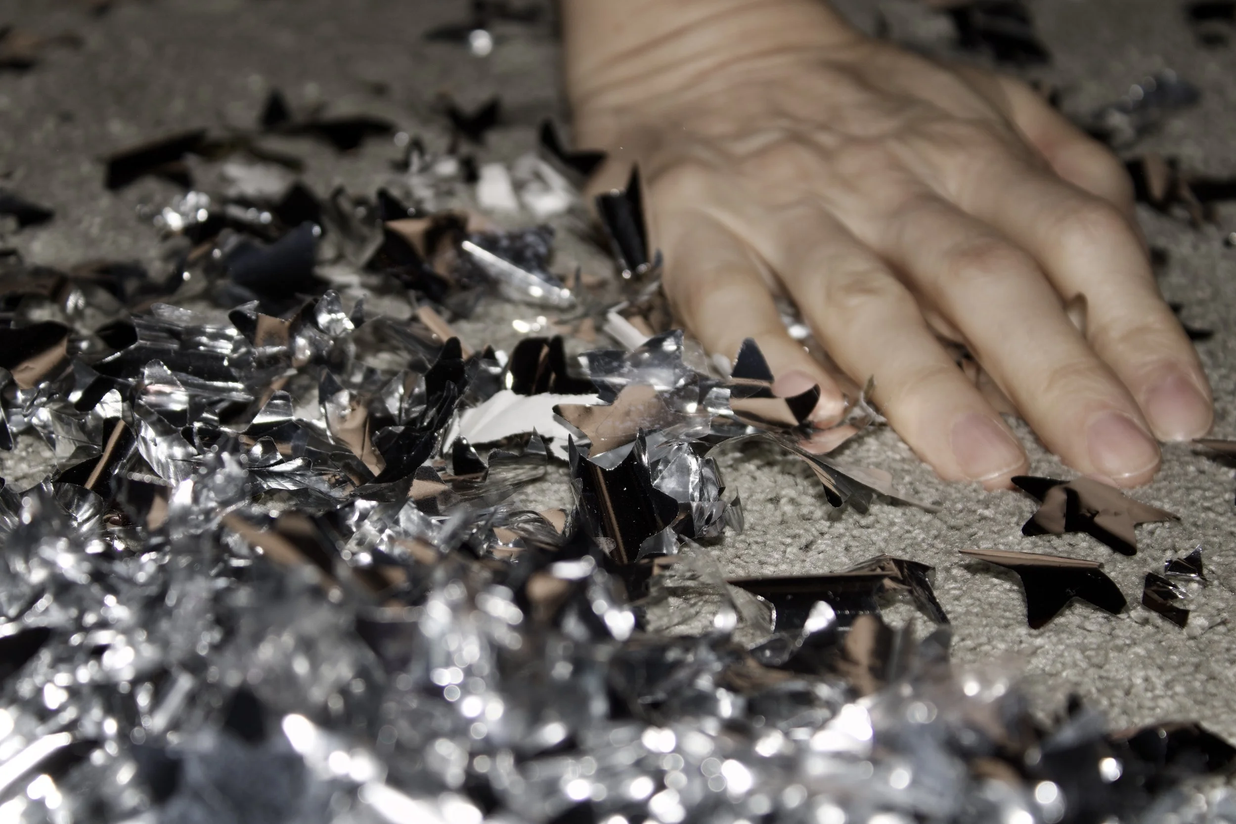 Close-up of shattered glass pieces on the ground with a human hand touching them.