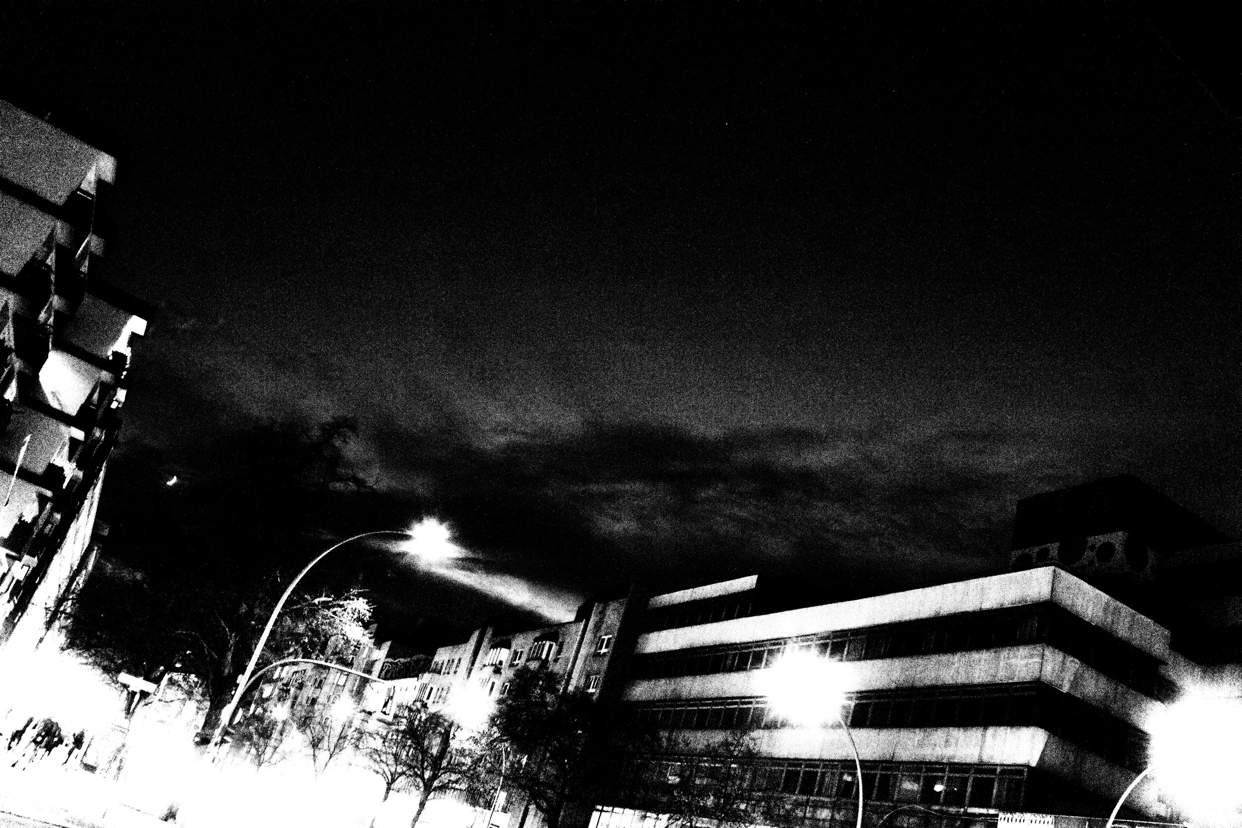 Nighttime cityscape with dark sky, some clouds, streetlights, and buildings with multiple windows