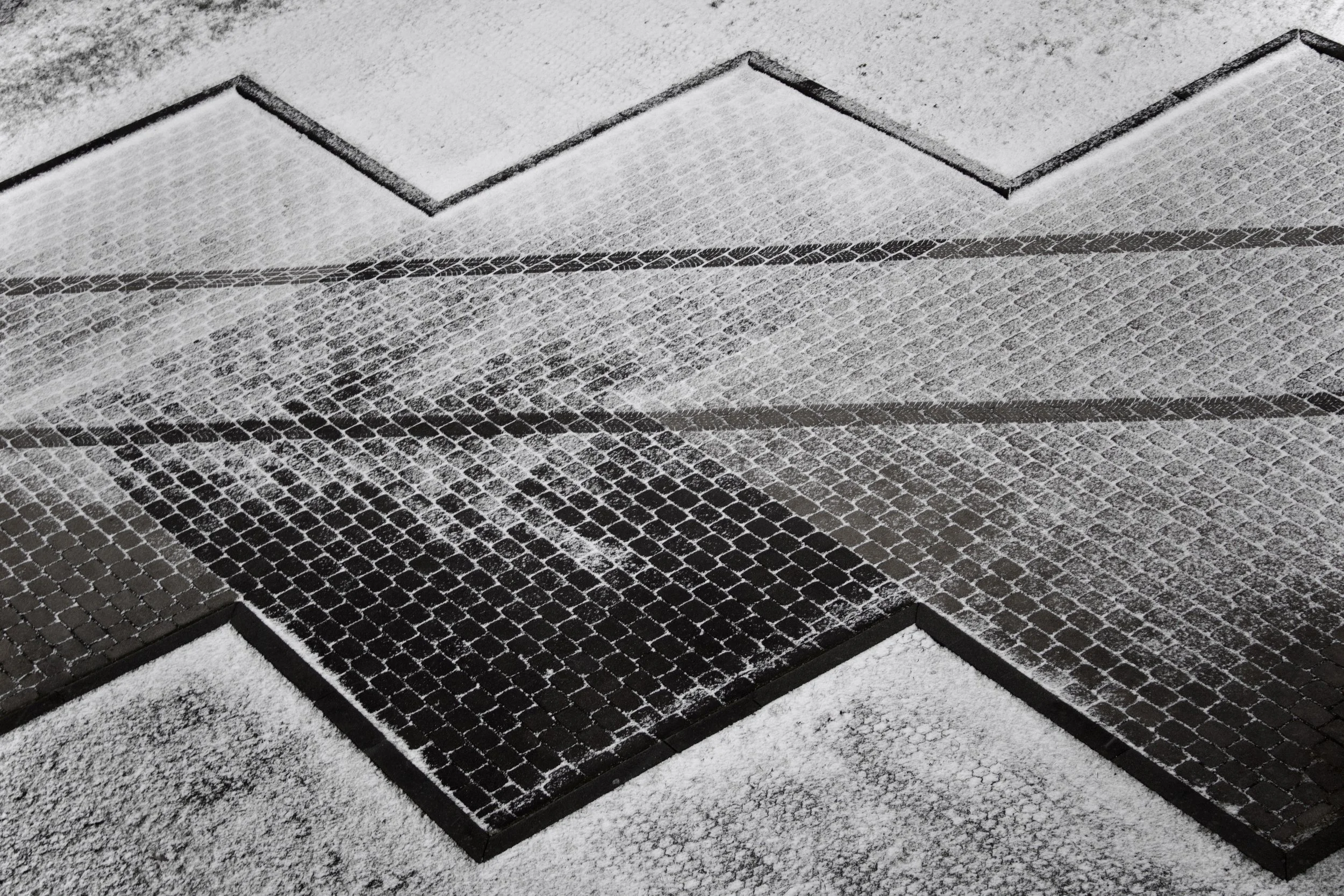 Black metal floor grates covered with light snow, arranged in parallel with a layer of snow around them.