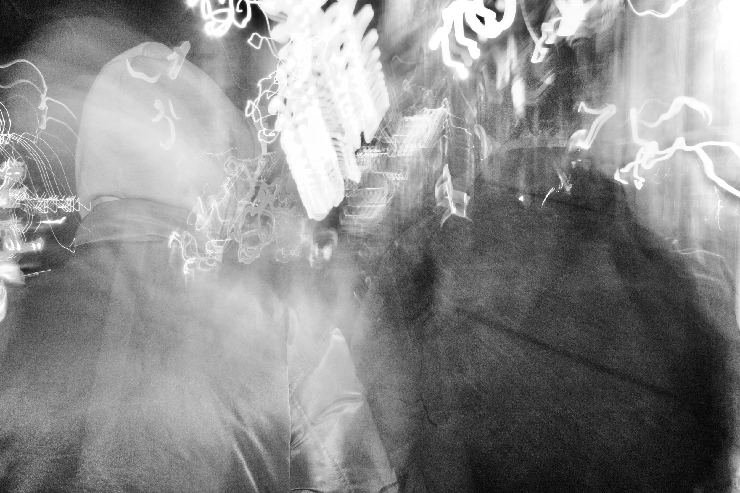 Black and white photo of blurred neon lights and reflections in what appears to be a city street at night.