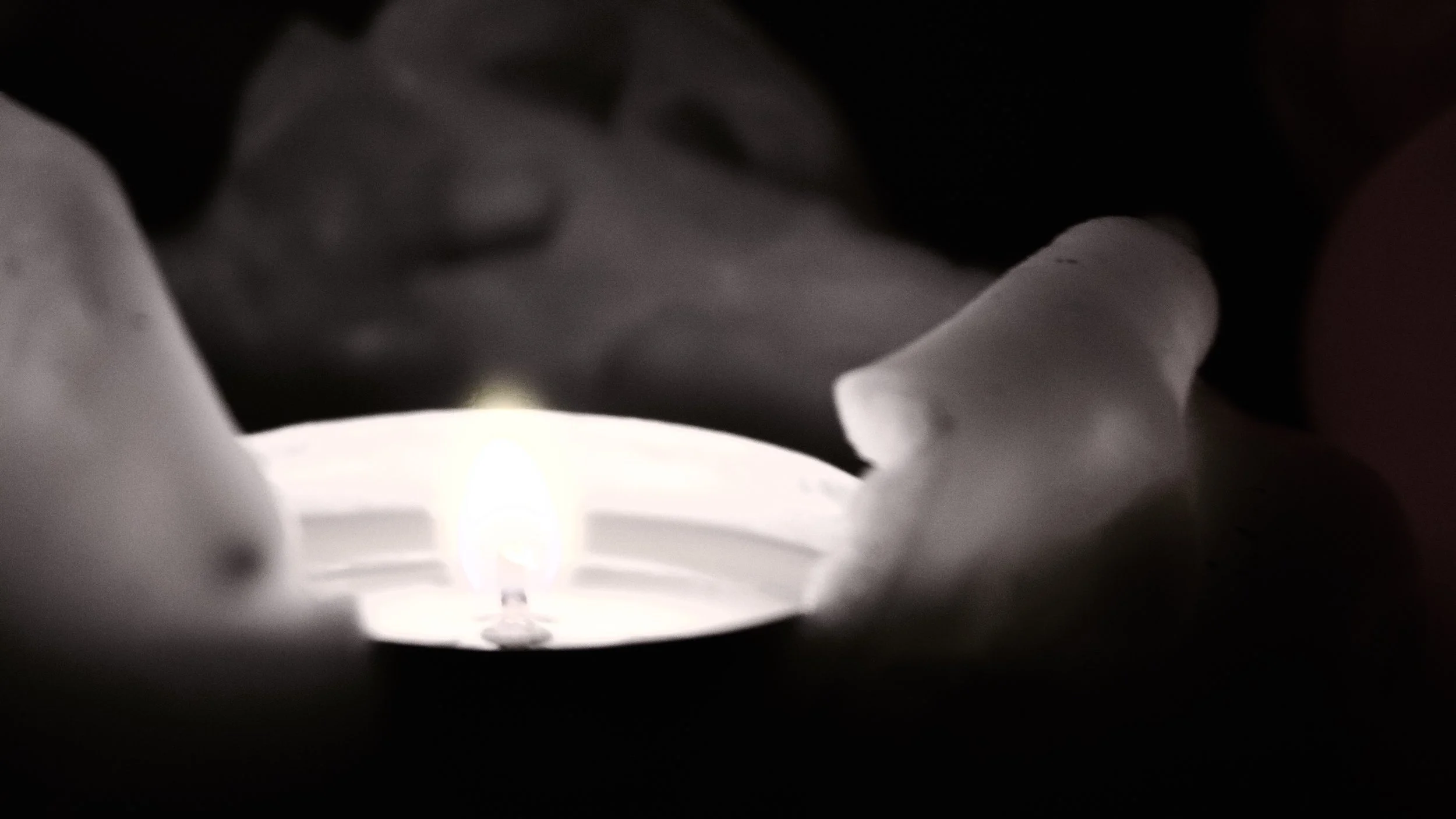 Close-up of a lit tealight candle in a white holder, with a dark background.
