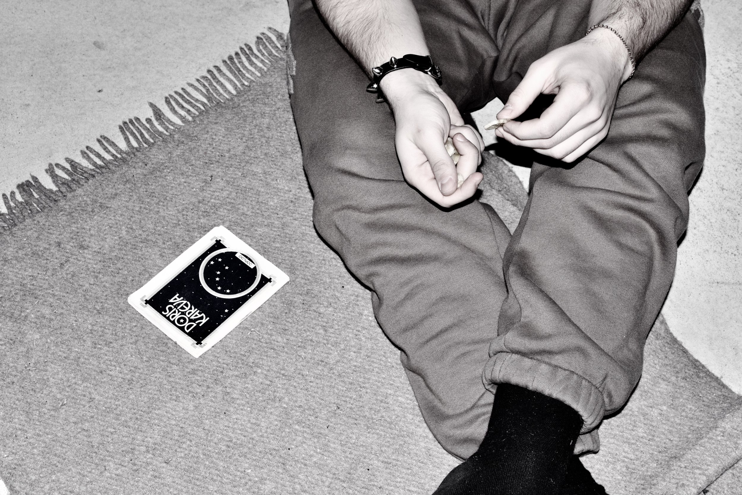 A person sitting on the ground holding a coin in their hand with a deck of playing cards, labeled 'Doris Karl', nearby on the ground.