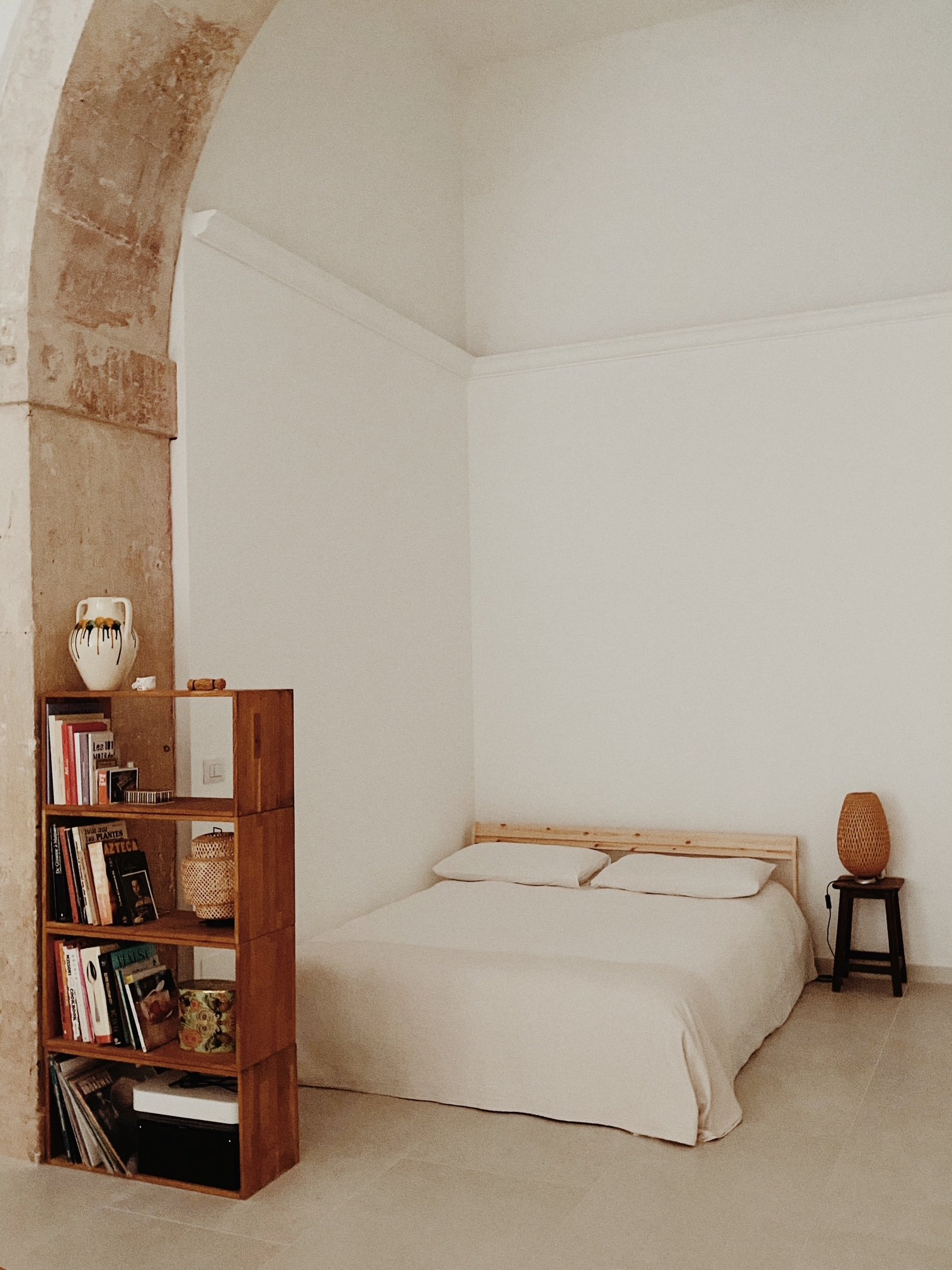 Bedroom with a bed, bookshelf, bamboo lamp, and a stone archway.
