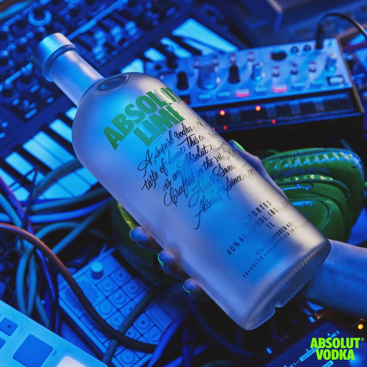 Frosted bottle of Absolut Lime vodka held in a neon blue music production studio with audio equipment