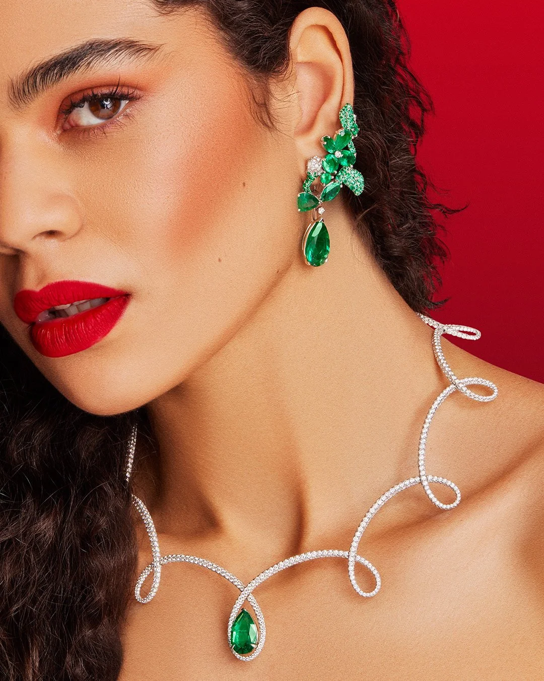 Woman wearing luxury pear-shaped emerald and diamond Faberge earrings with a matching swirling diamond necklace.