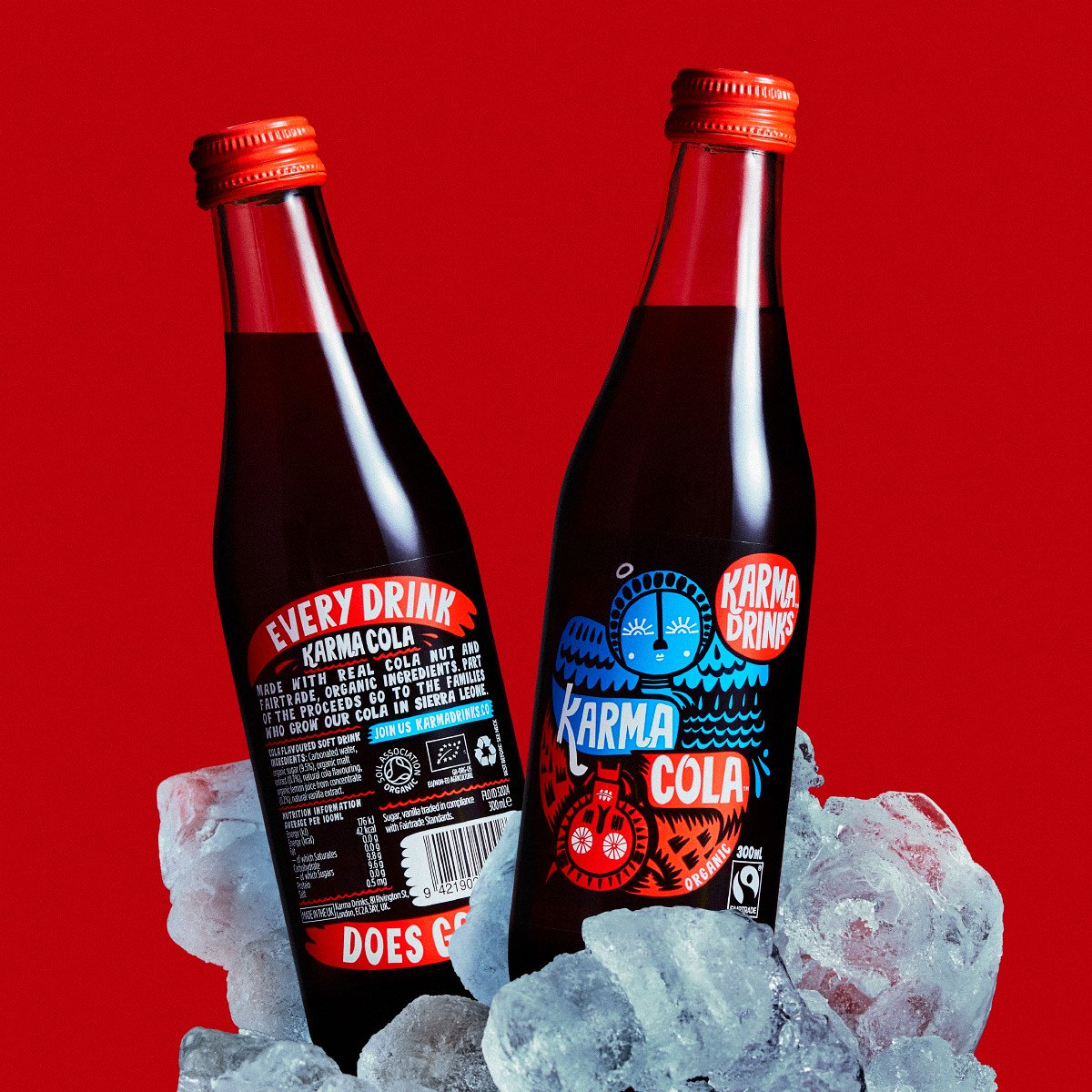 Two Karma Cola organic glass bottles resting in a pile of ice cubes against a bright red background.