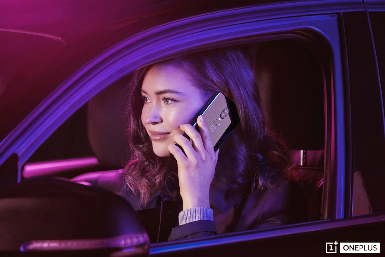 Woman talking on a OnePlus smartphone while sitting in a car with purple and pink neon lighting at night.