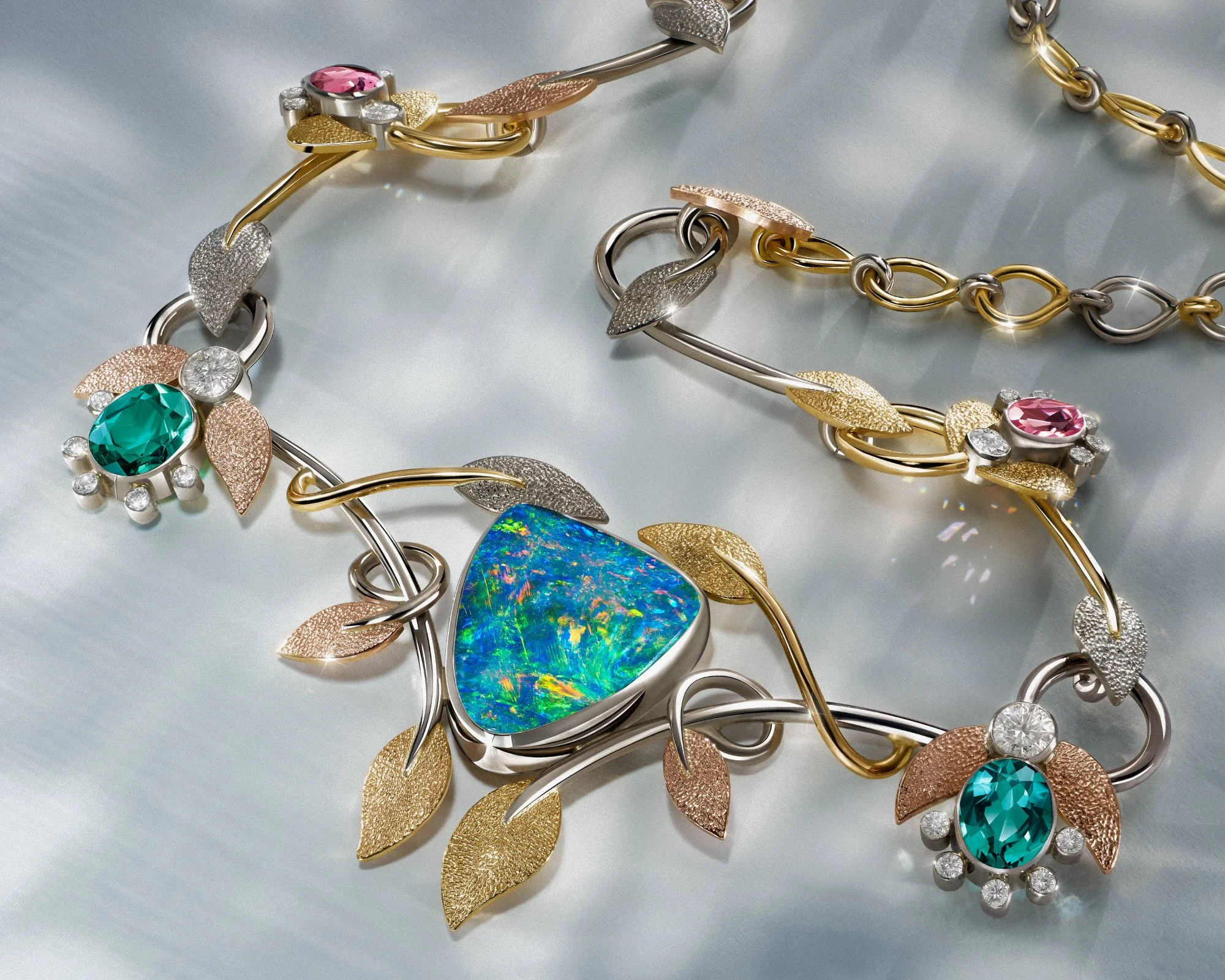 Intricate opal and gold leaf necklace with emeralds and pink sapphires on a silver background.