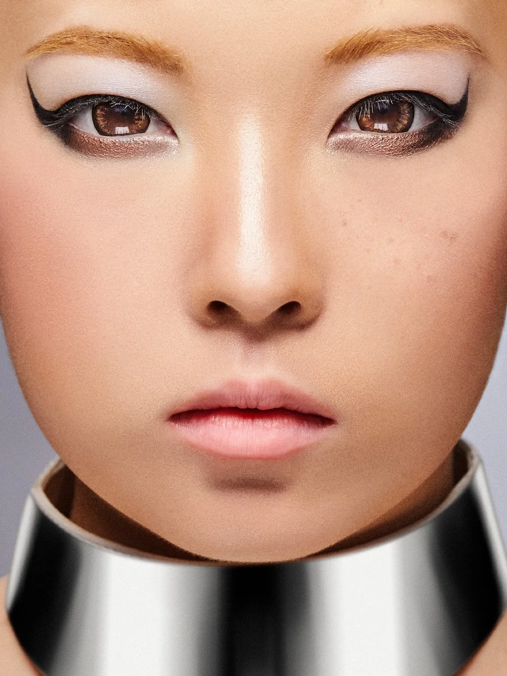 Close-up of an Asian woman with winged eyeliner, blonde eyebrows, and a thick silver metallic choker collar-Mac cosmetics