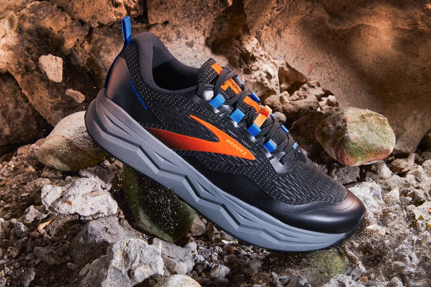 Black and orange Brooks Caldera trail running shoe positioned on rugged rocks commercial studio photography