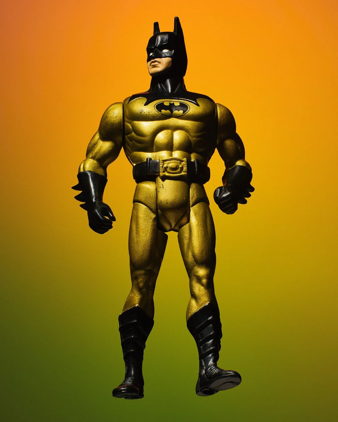 Gold and black Batman action figure standing against a vibrant orange and green gradient background.