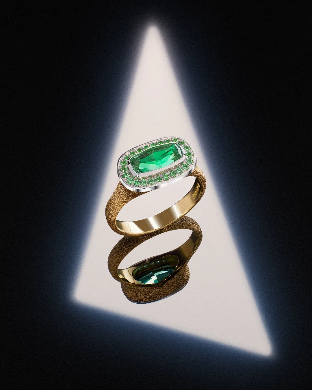 Gold ring with a large central emerald and halo of green gems on a textured band, reflected in light.