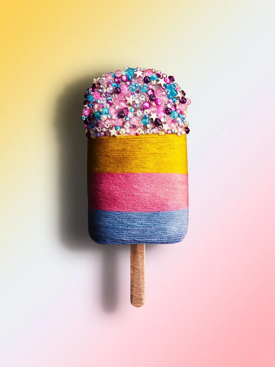 A decorative popsicle made from multi-colored yarn and topped with sparkling beads and stars.