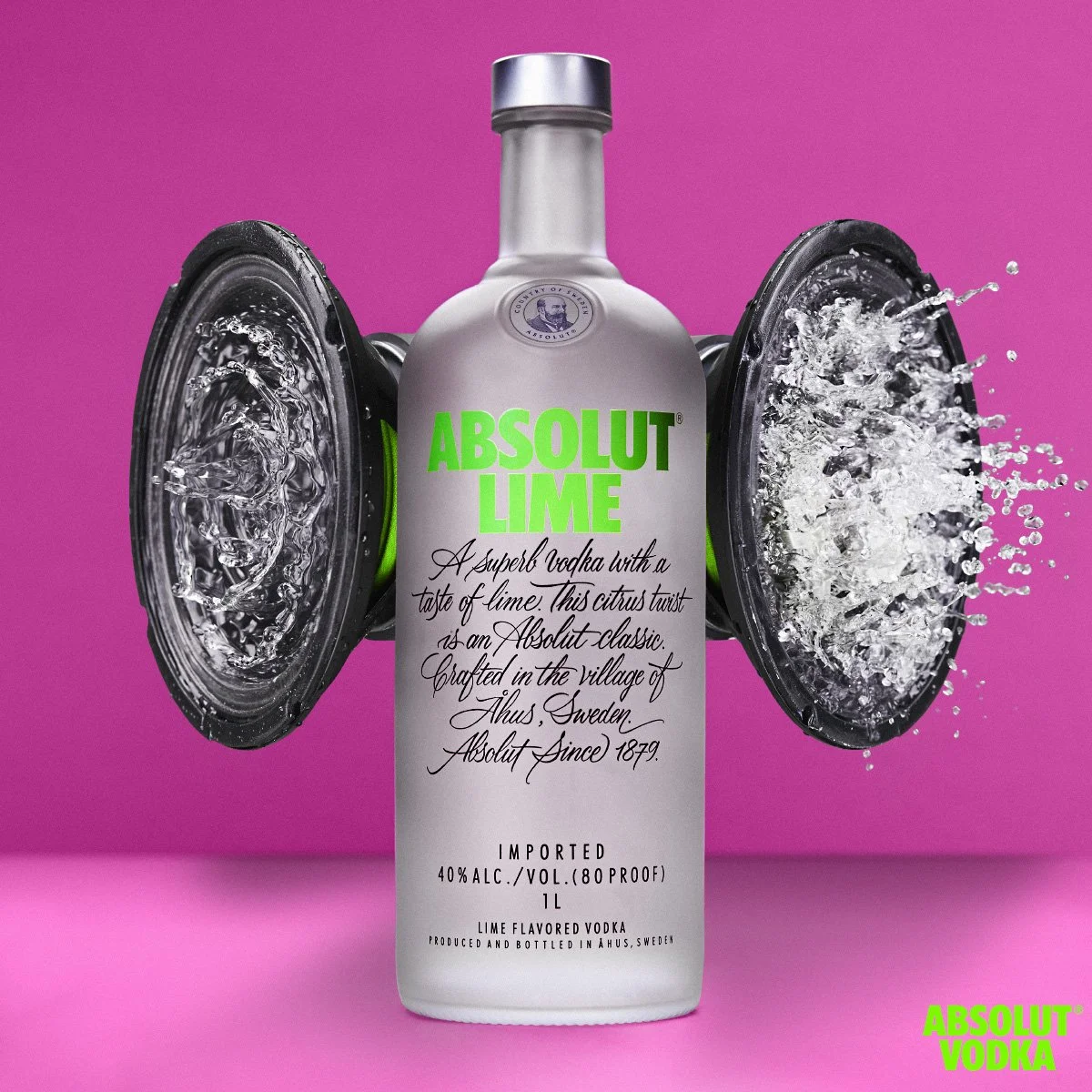 Absolut Lime vodka bottle centered between two speakers with water splashing out against a bright pink background.