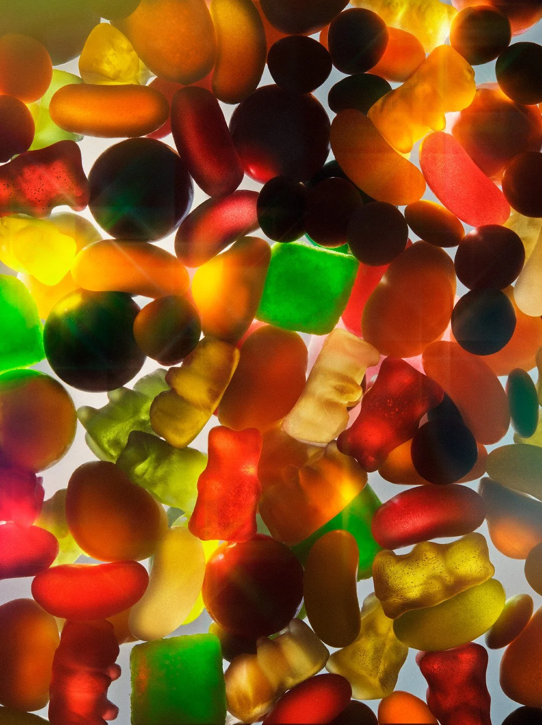 Backlit translucent gummy candies including bears and jelly beans in various vibrant colours like red, green, and yellow.
