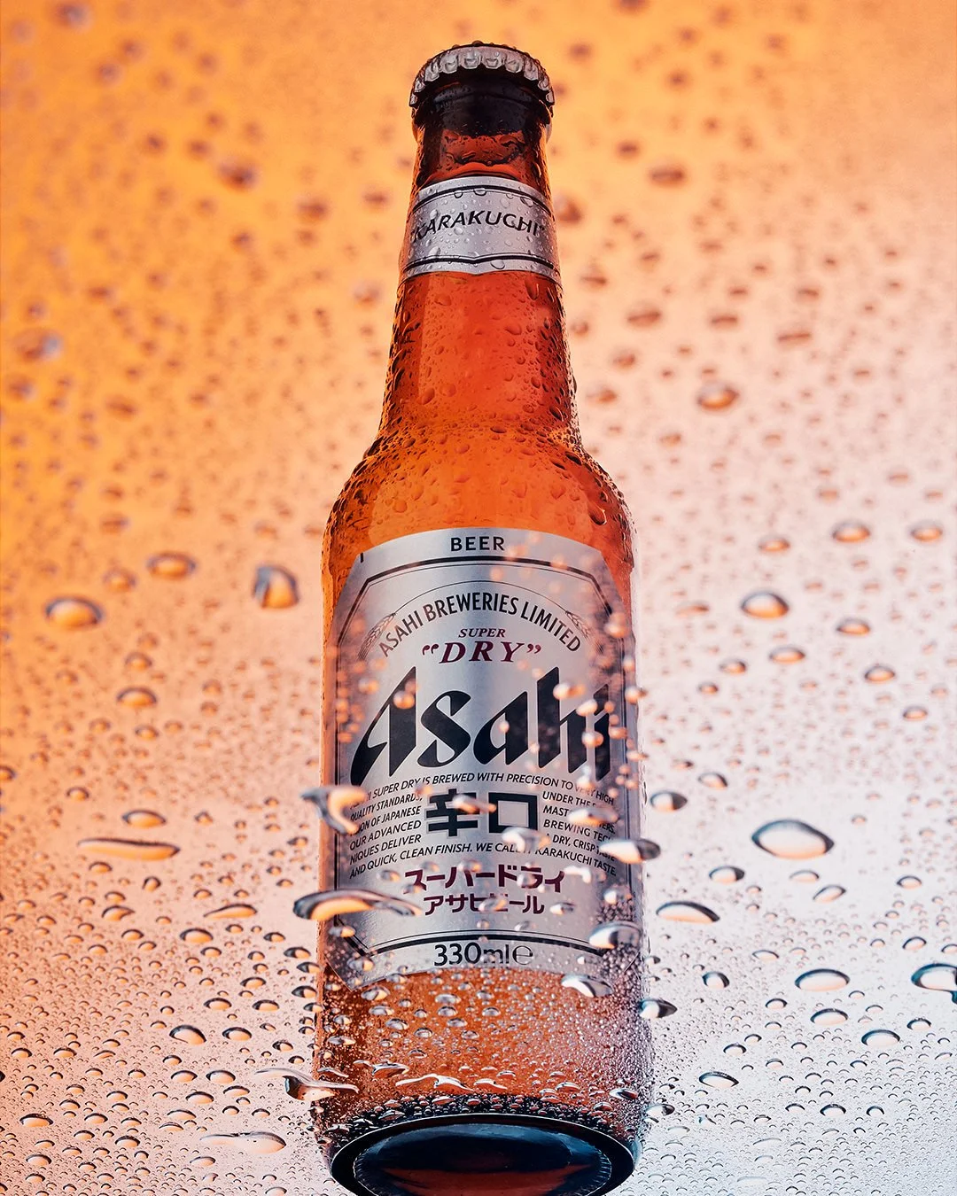 A cold bottle of Asahi Super Dry beer covered in condensation against an orange background with water droplets.