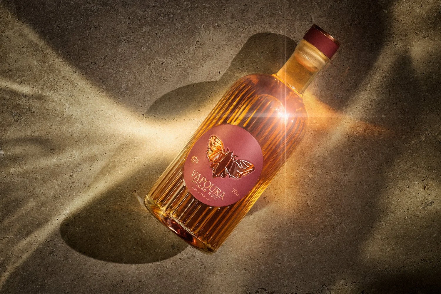 Vapoura Spiced Rum bottle on a stone surface with dramatic golden sunlight and palm leaf shadows.