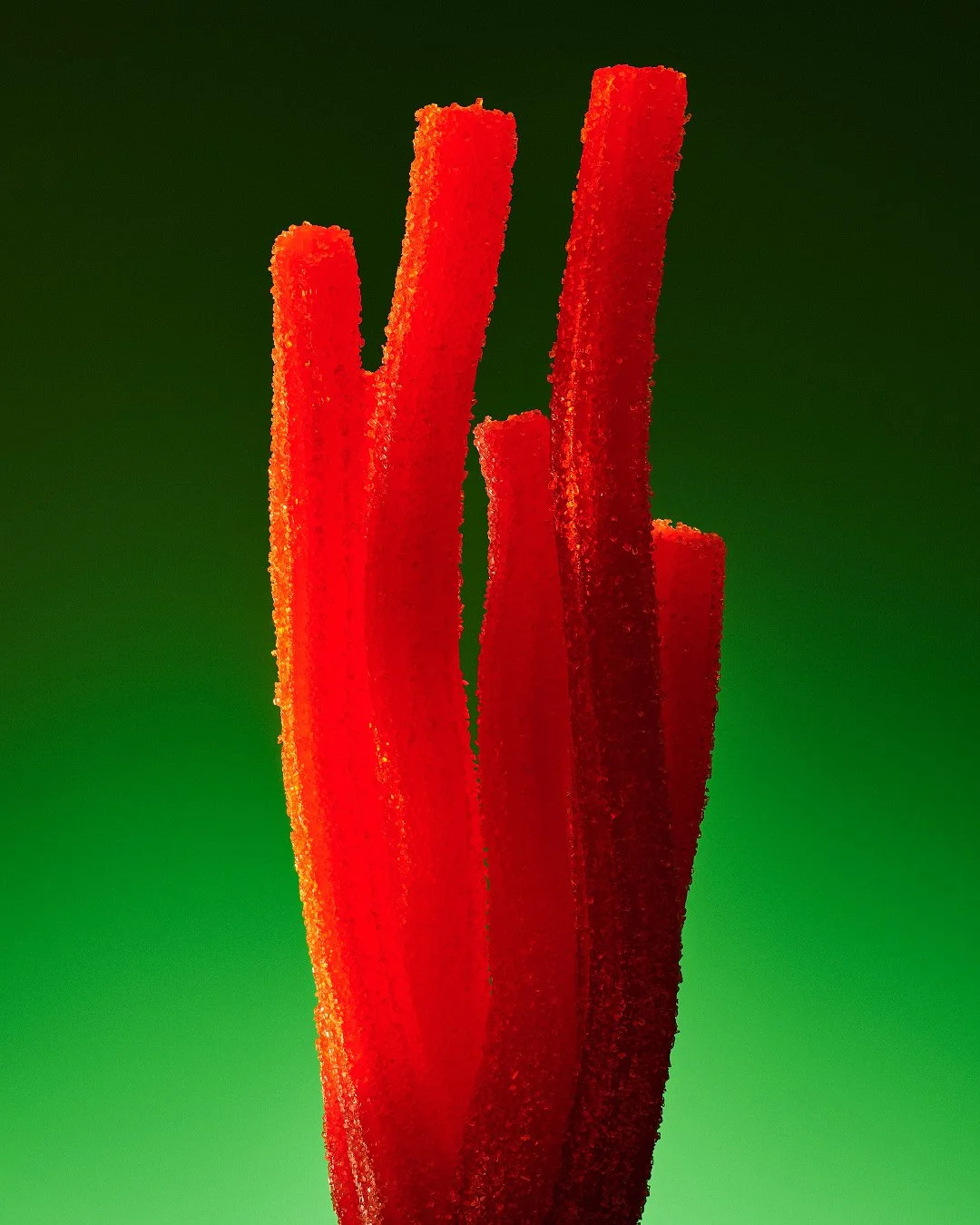 A bundle of red sugar-coated sour candy strips standing vertically against a vibrant green gradient background.