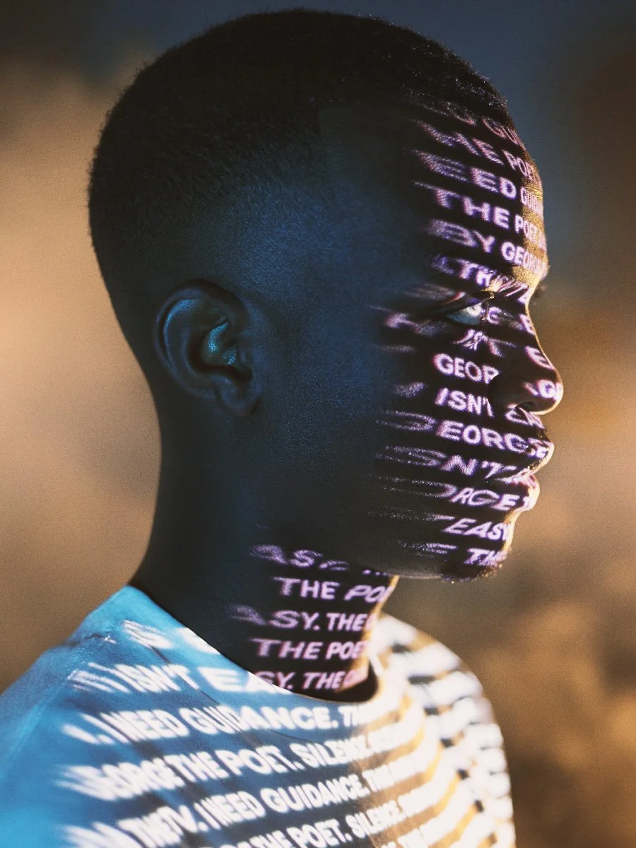 Side profile of a Black man with purple and white text projected onto his face and neck under cinematic blue lighting