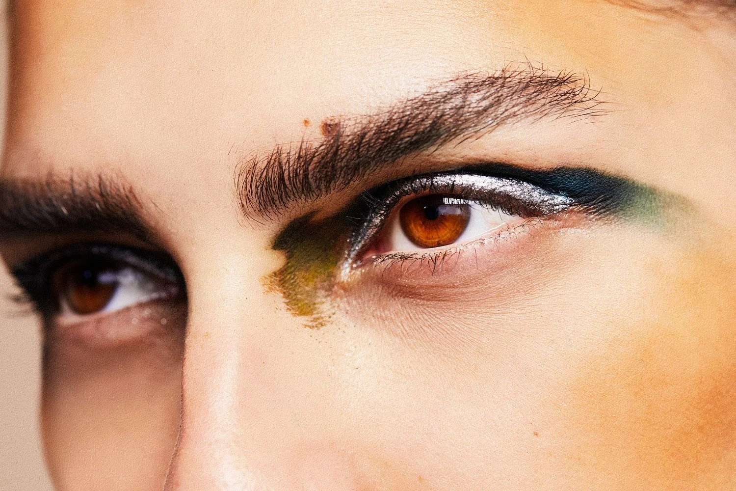 Close-up of a hazel eye featuring dramatic silver glitter eyeliner and thick dark eyebrows-Mac cosmetics