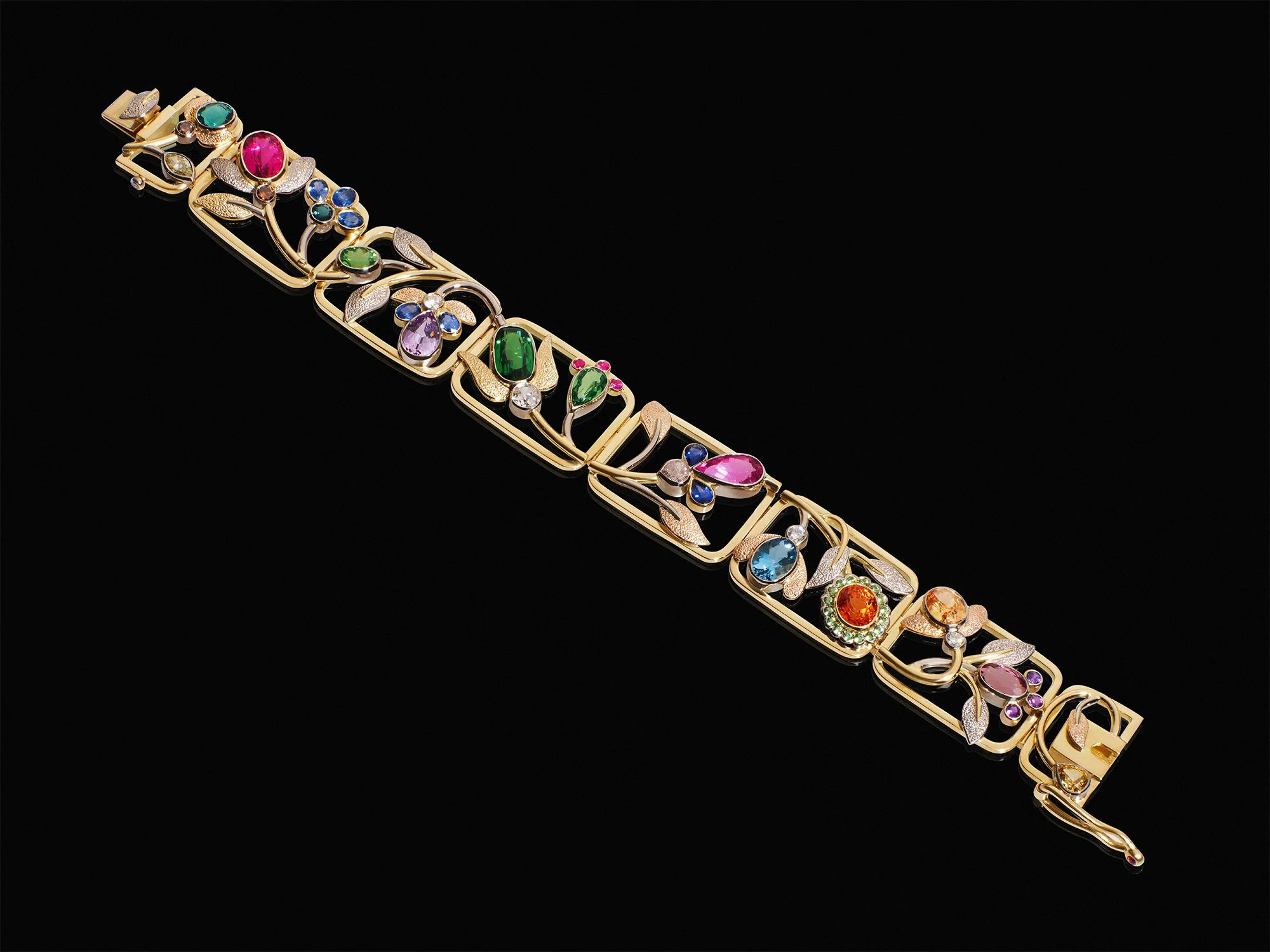 Luxury gold link bracelet featuring colourful multi-gemstone floral designs on a black background.