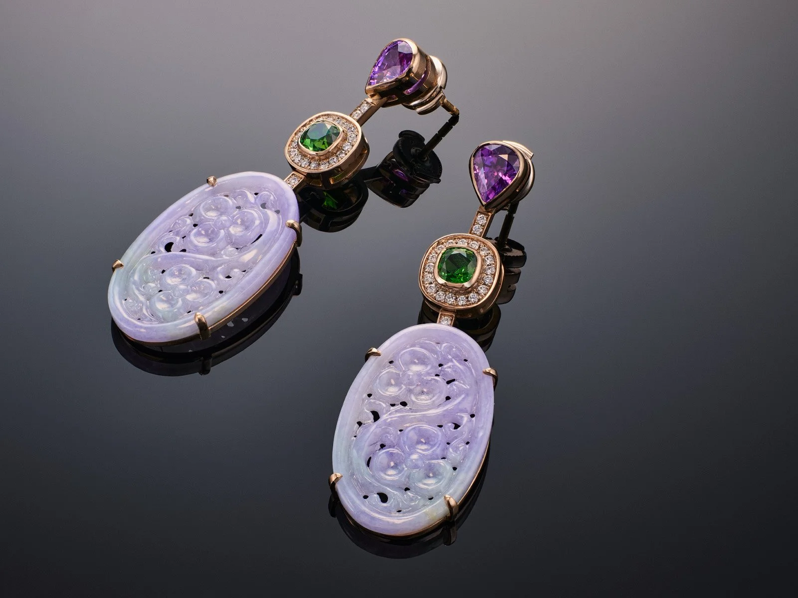 Ornate drop earrings featuring carved lavender jadeite, green emeralds, and purple amethyst in a gold setting