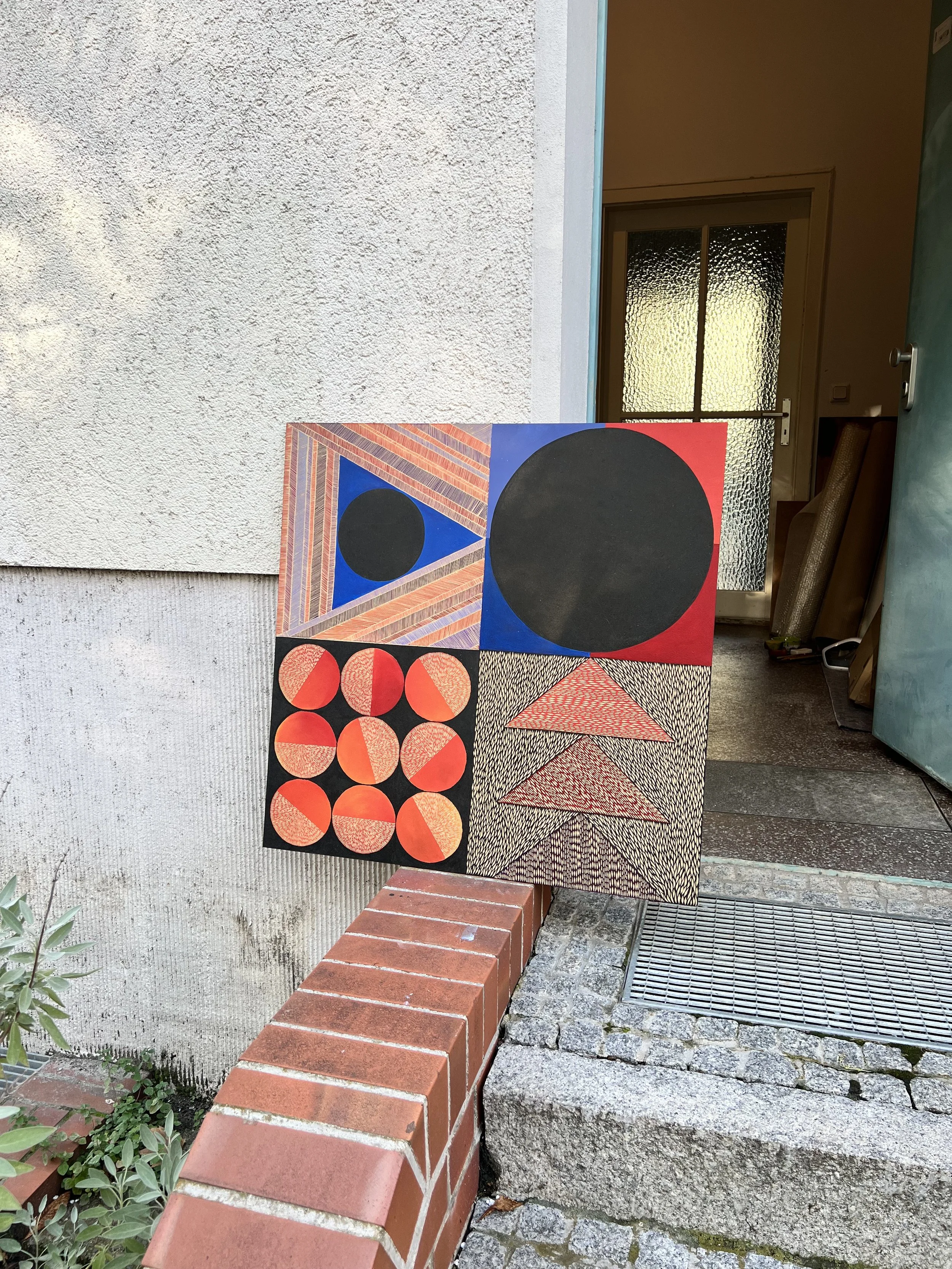 Geometric abstract art panel with various shapes and patterns leaning against a wall near a brick step.