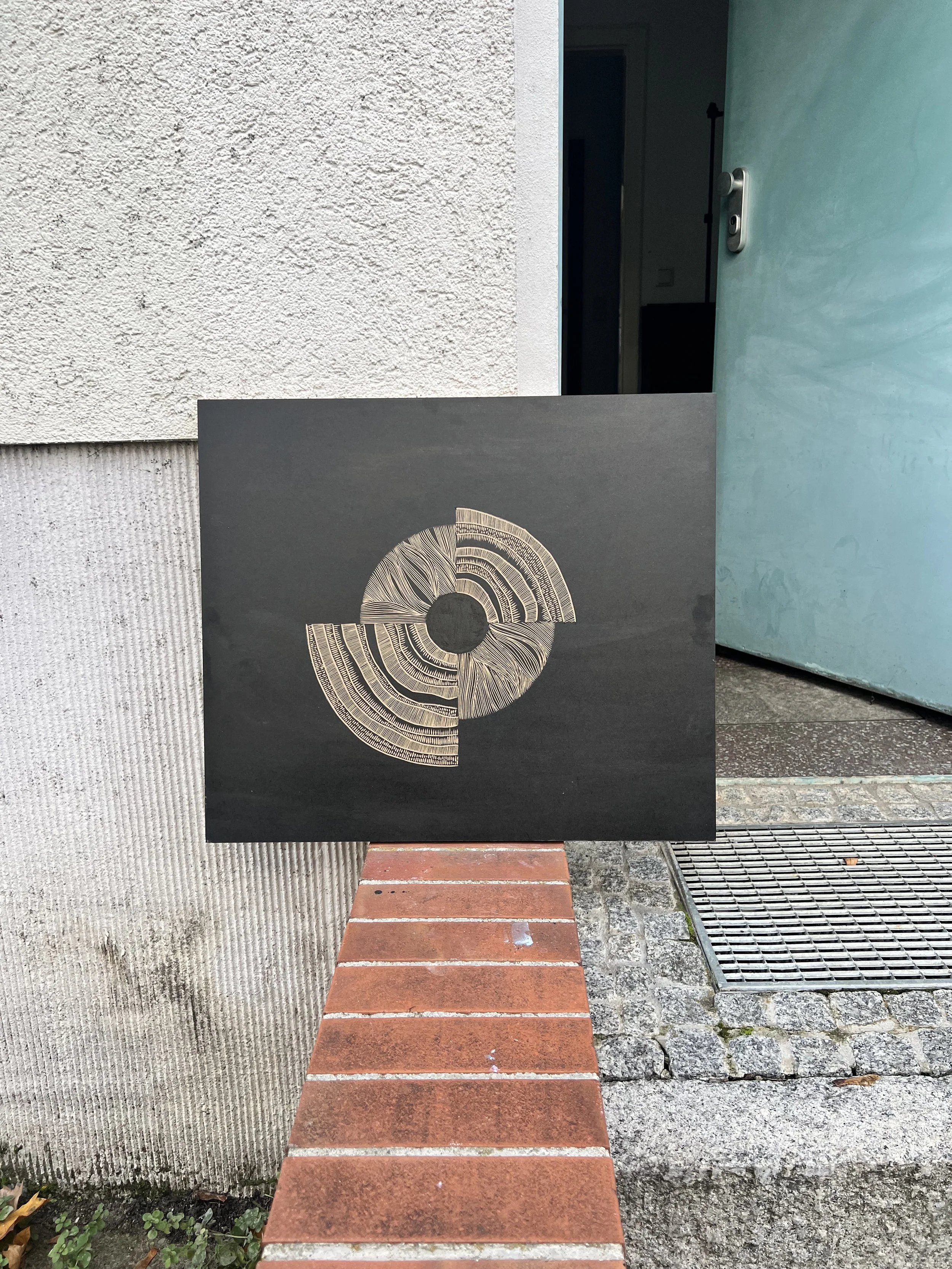 Abstract artwork on a black canvas with a circular design in light brown, leaning against a textured wall near an open blue door.