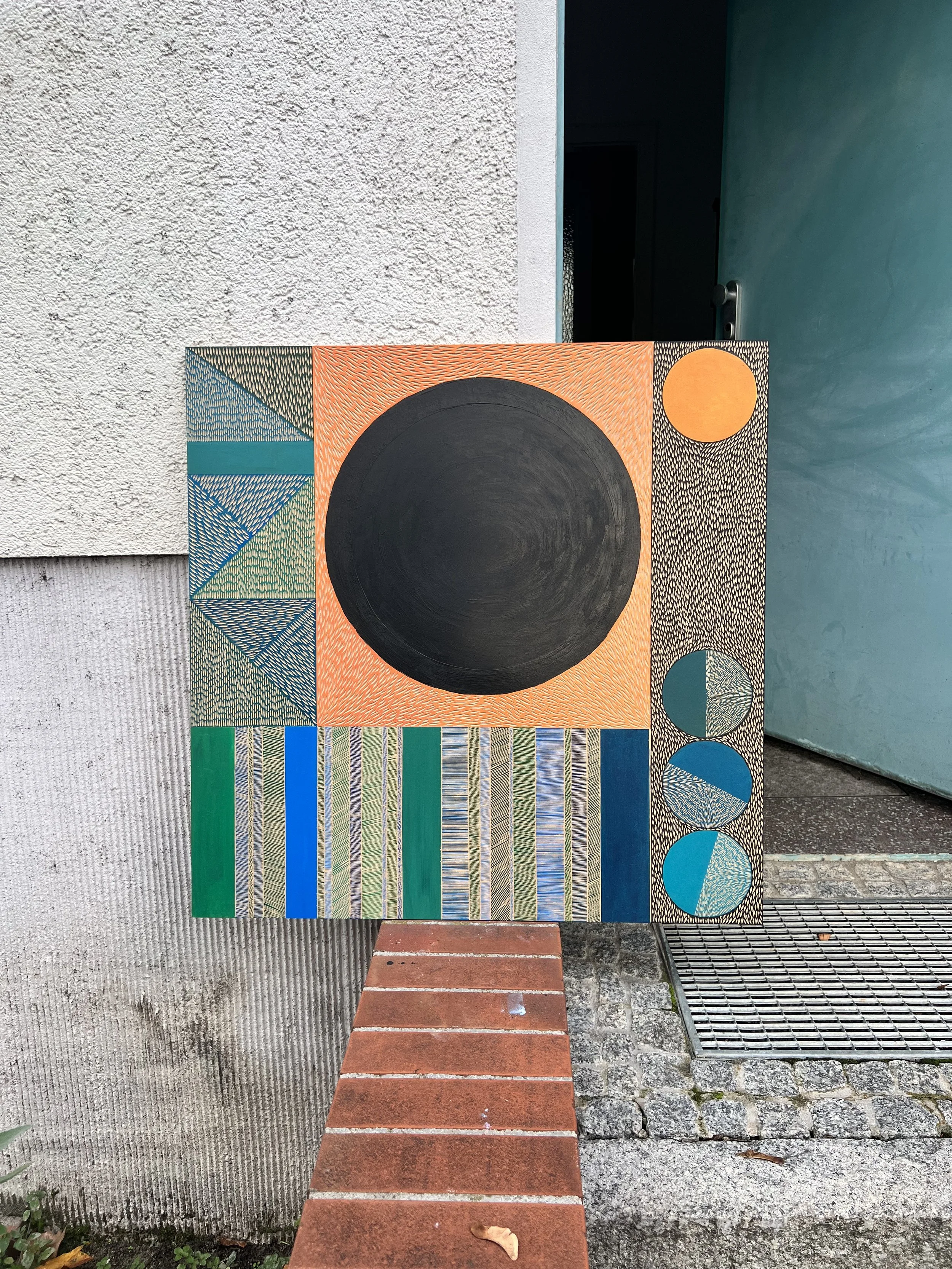 Abstract painting with geometric shapes, featuring a large black circle, orange and blue patterns, and vertical striped sections in green and blue tones, displayed against a textured white wall and blue door.