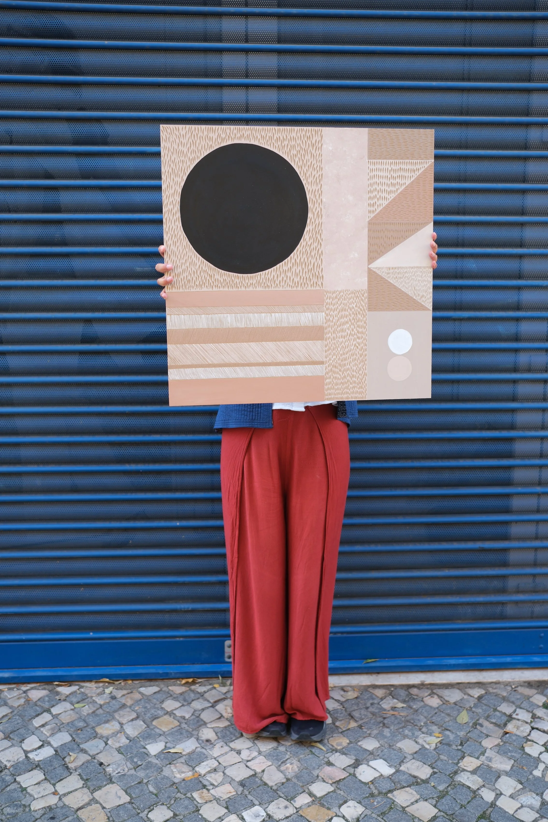 Person holding abstract geometric art in front of blue metal shutter