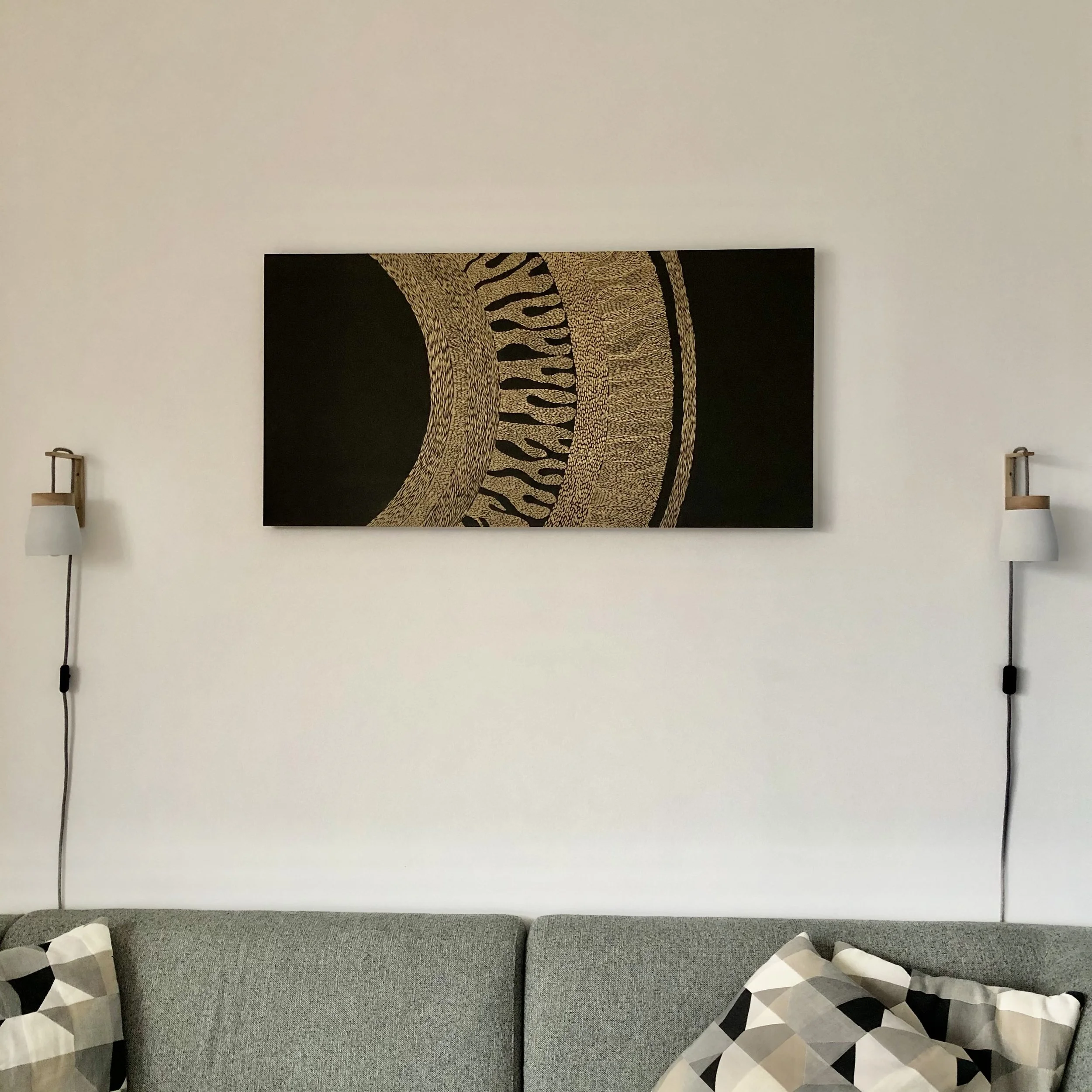 Minimalist living room with abstract art piece above a gray sofa, flanked by wall sconces and decorative pillows.