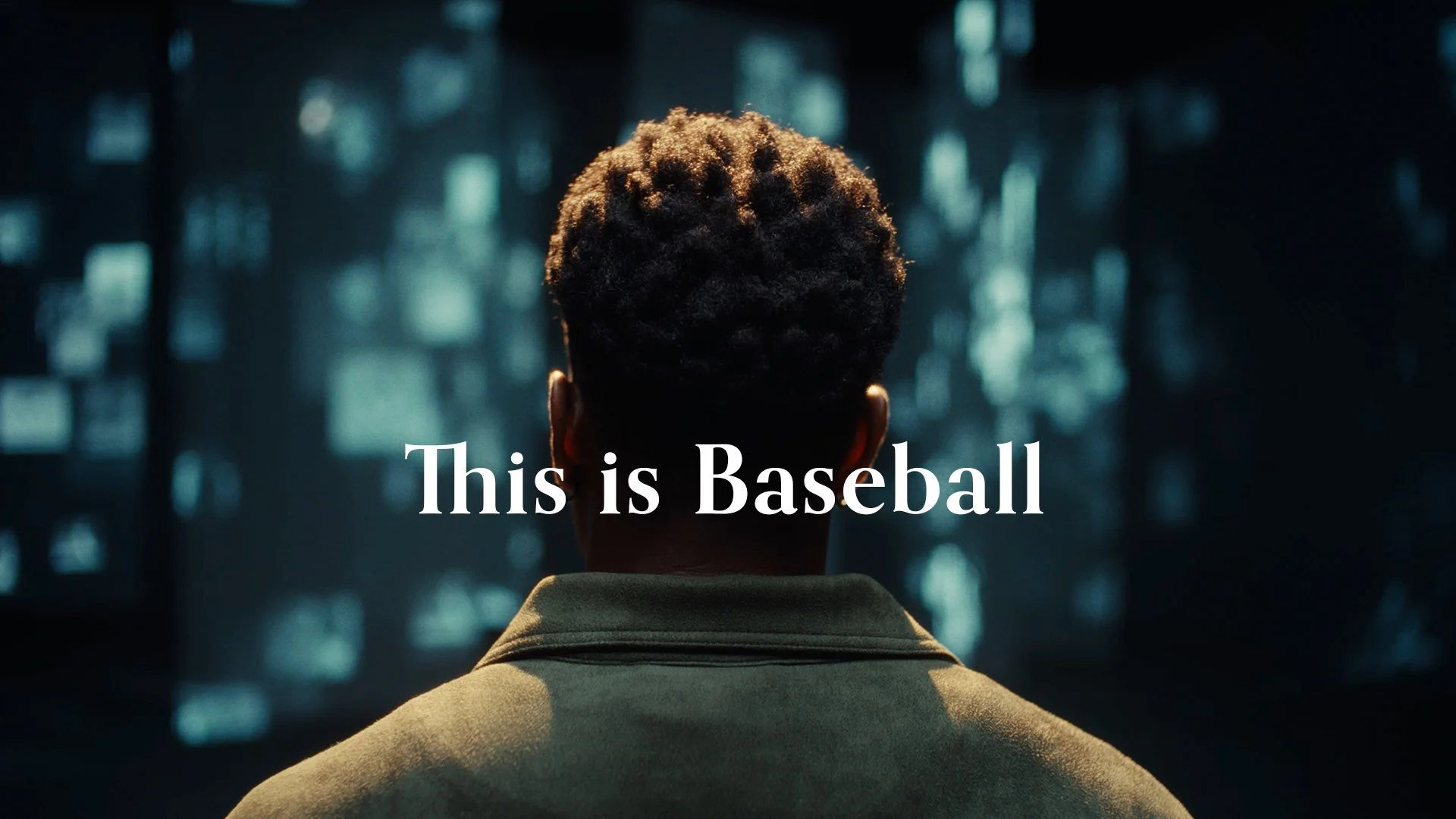 A person with short, curly hair viewed from behind, looking at a dark background with blue lights. Text overlay reads 'This is Baseball'.