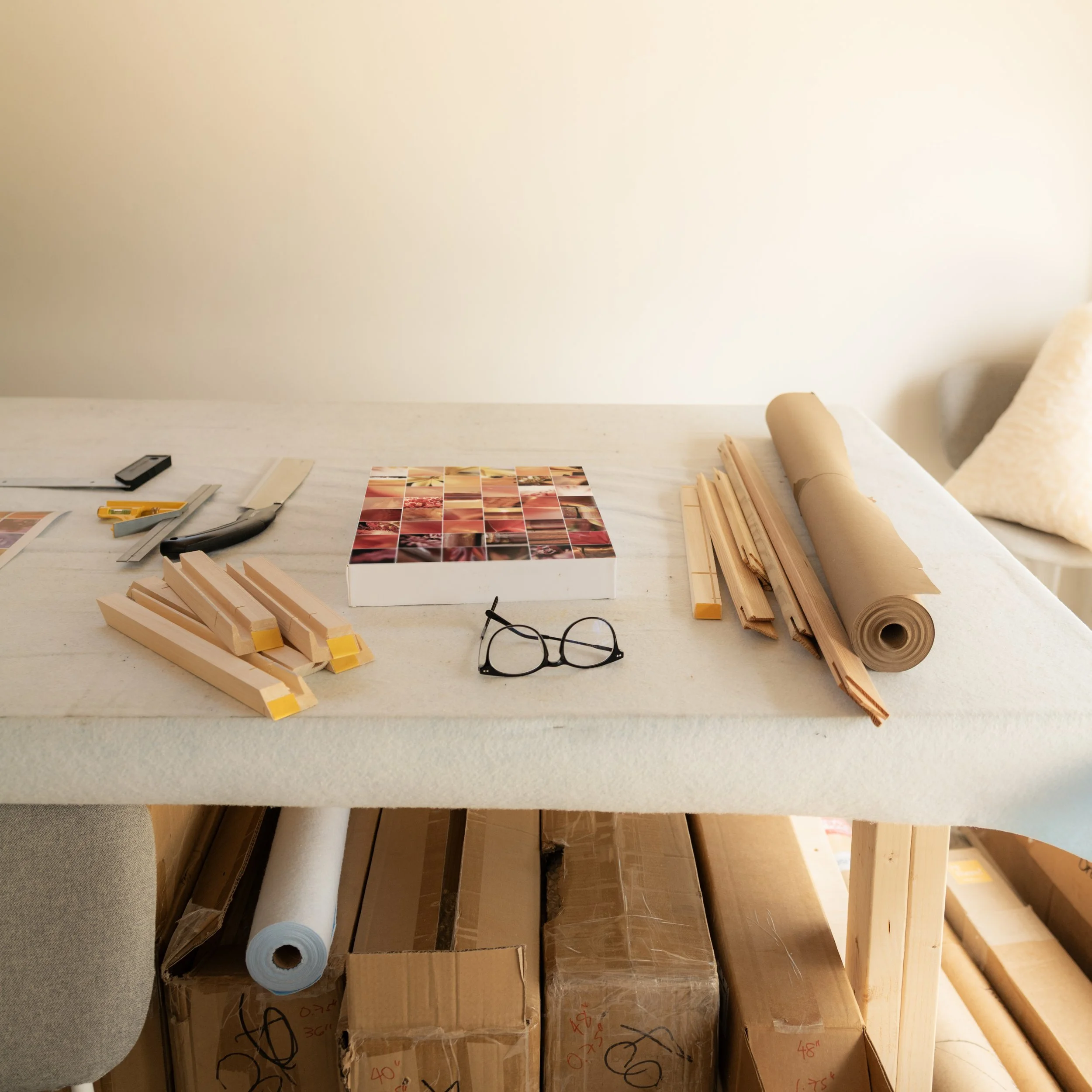 A piece of artwork sits on a work table with various framing tools around it.