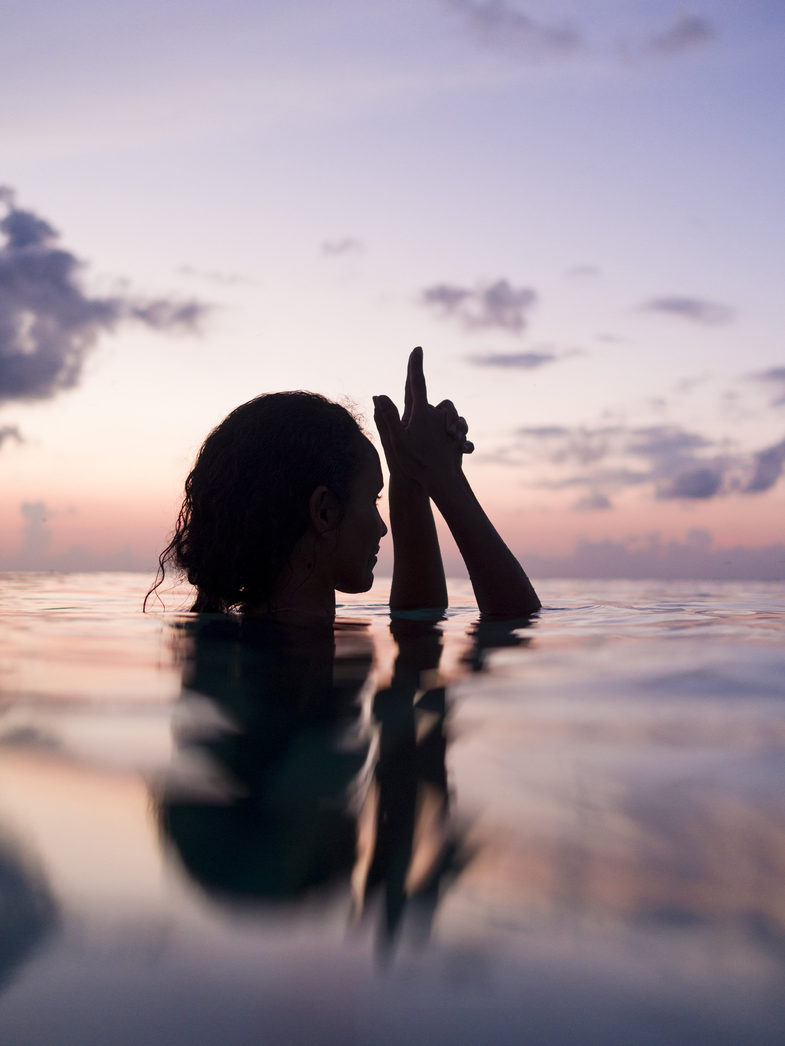 Silhouette of a woman in water during sunset with hands in prayer position.