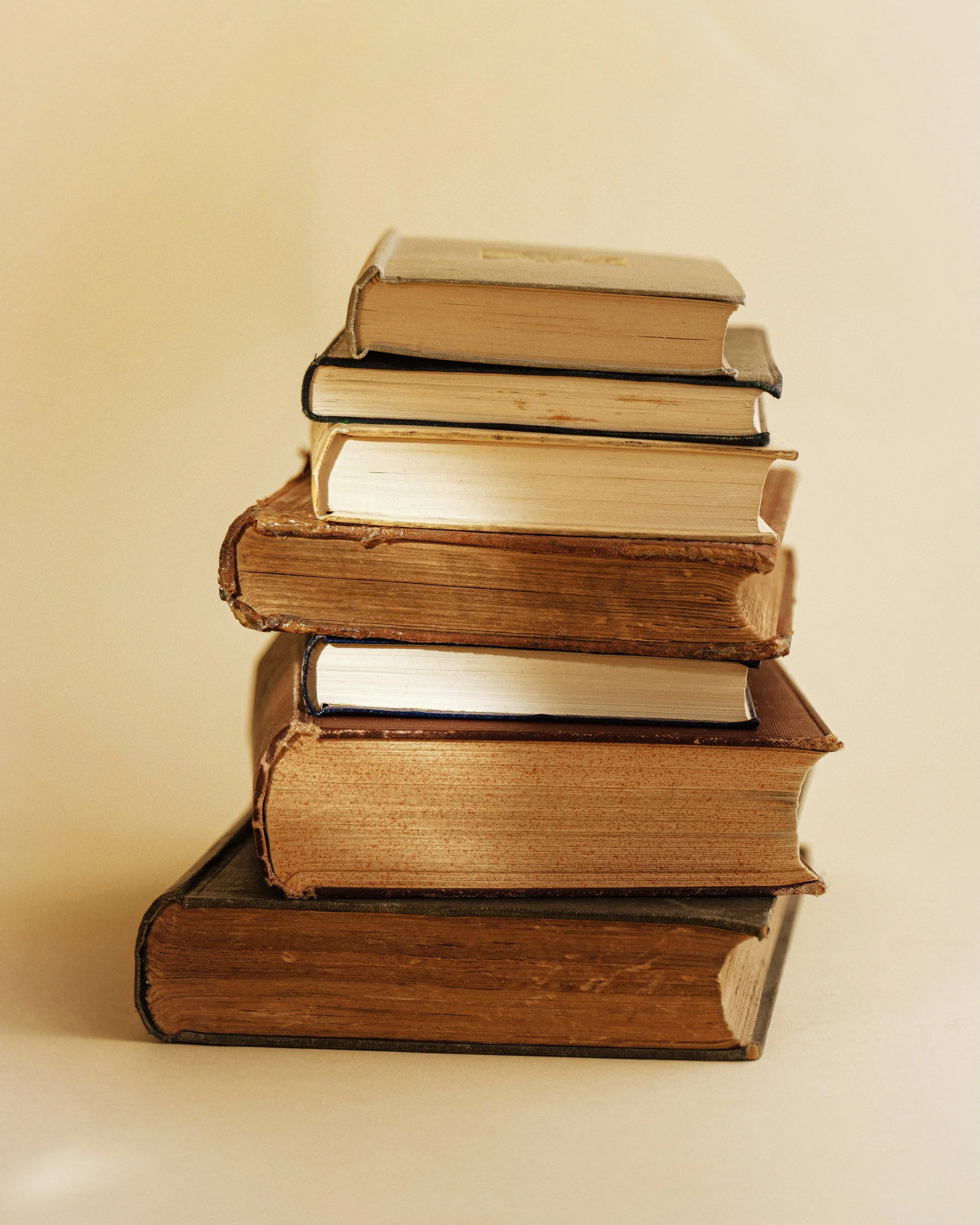 A stack of seven old and new books on a beige surface with a beige background.