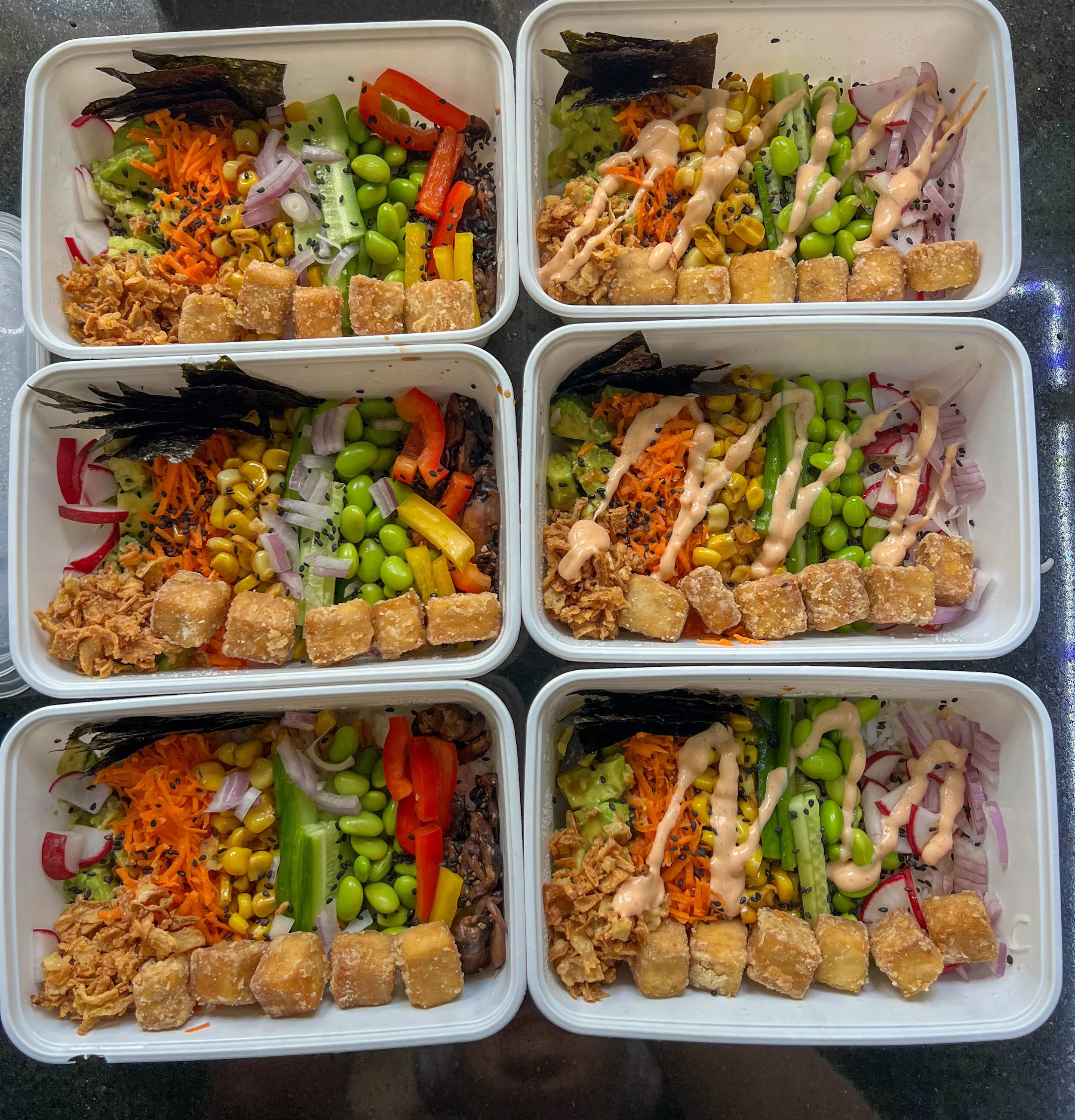 Rectangular bowls full of a rainbow of veggies, sauce, and tofu