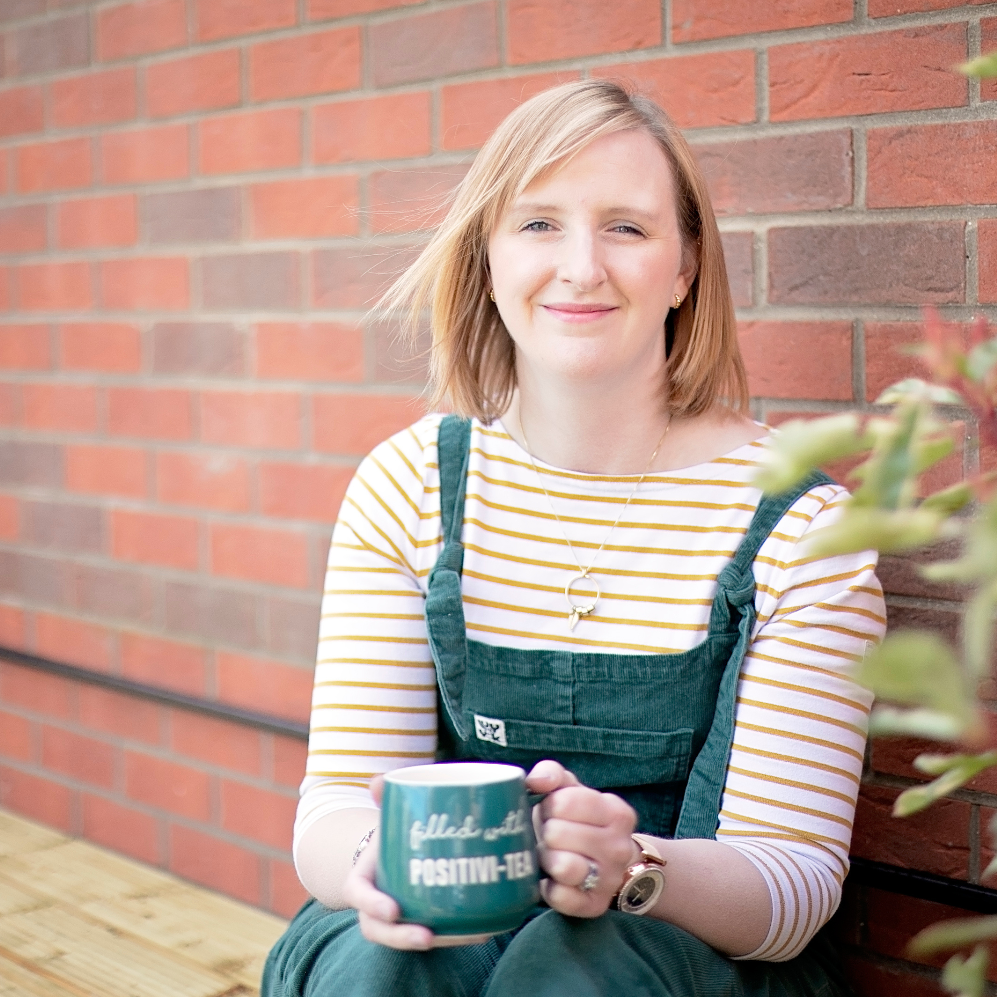 A blonde woman sits outside drinking a cup of tea