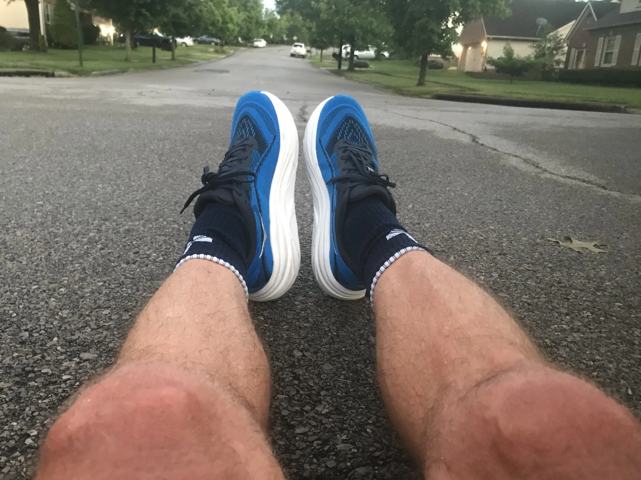 Closeup of man sitting on wet road wearing HOKA Skyflow running shoes