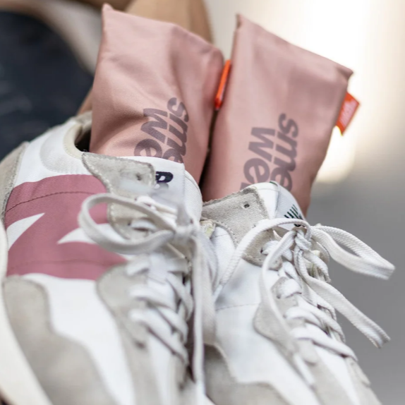 A pair of white New Balance sneakers with pink accents and two pink Smellwell bags placed in the shoes.