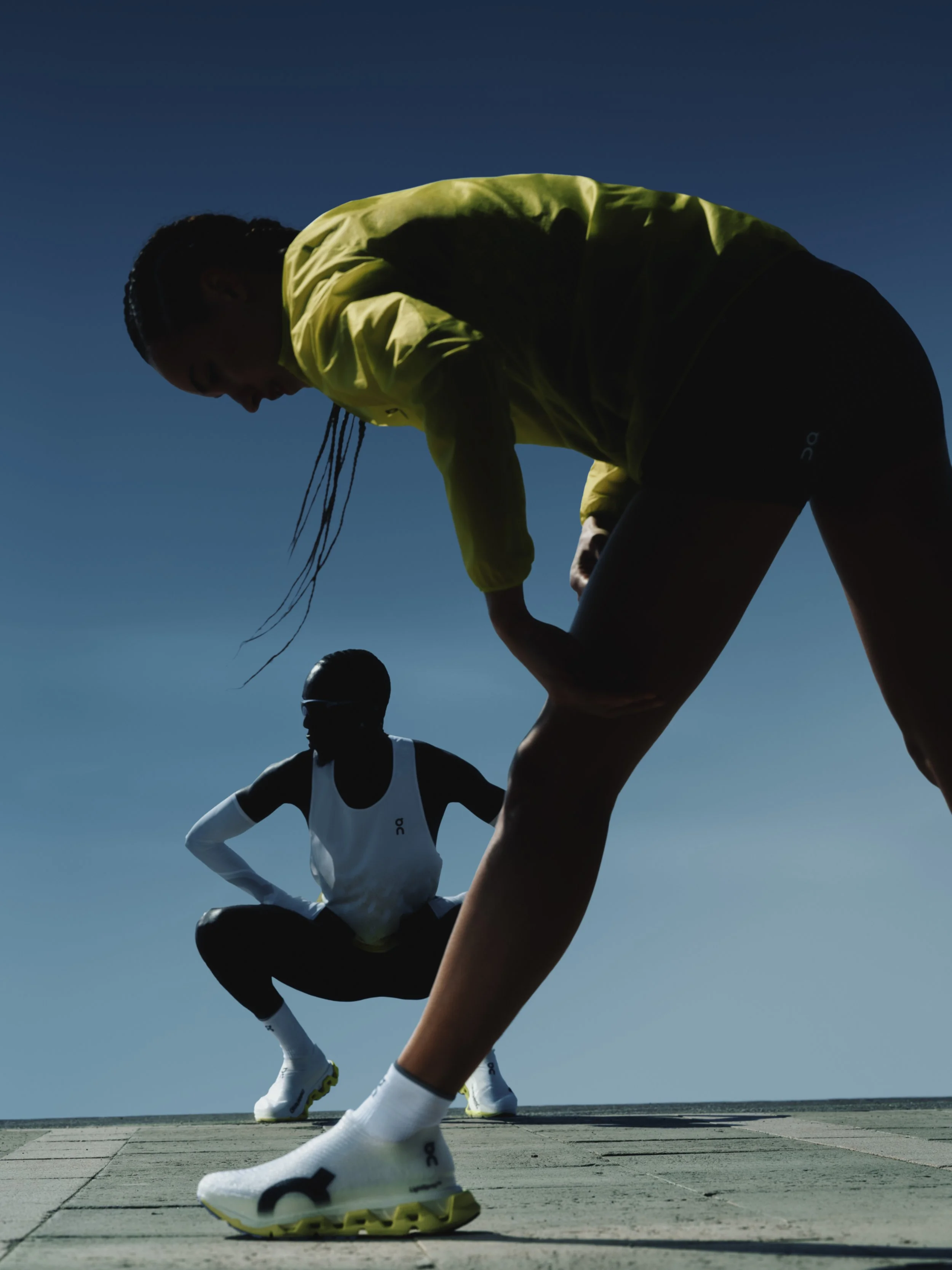Woman and man stretching while wearing Closeup of On LightSpray Cloudmonster 3 Hyper