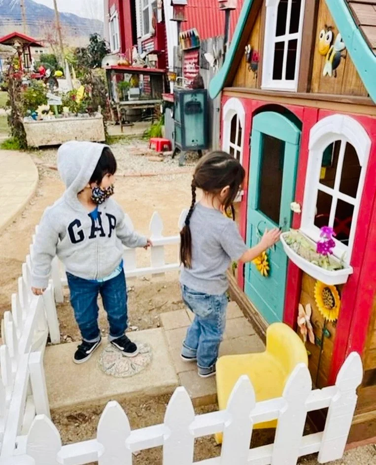 Two children standing outside a colorful playhouse in a garden.