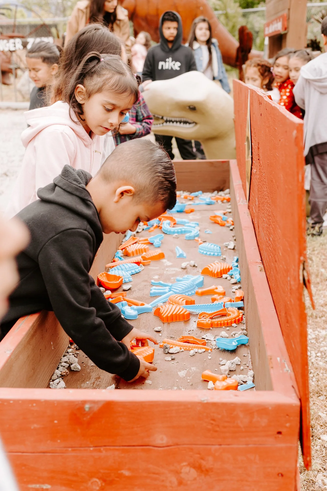Children playing a game with orange and blue whale-shaped cookie cutters on a wooden table outdoors.